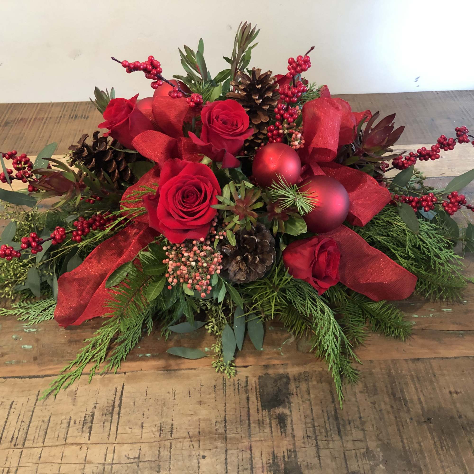 Red roses with pinecones, berries, and ribbon in a low holiday arrangement
