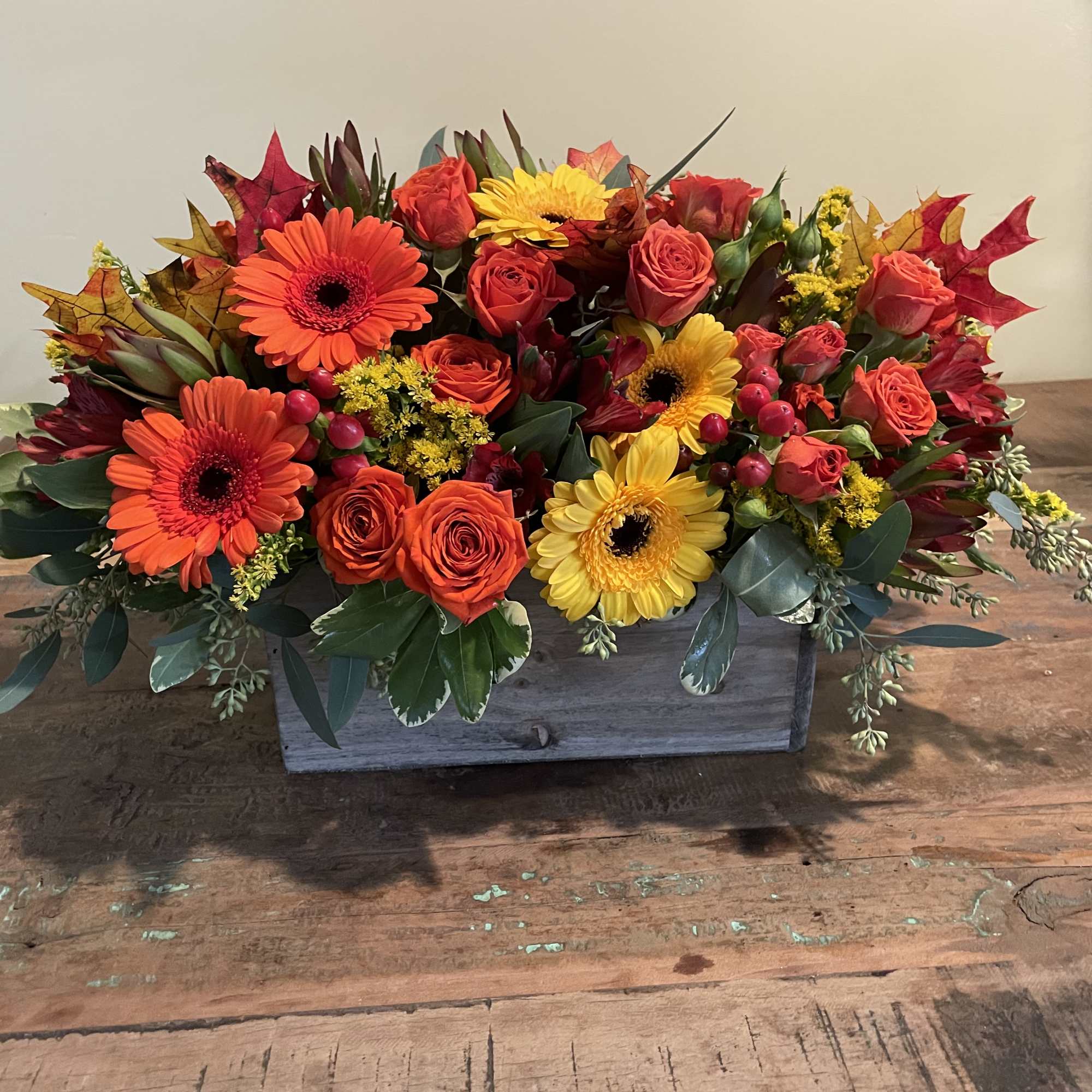 Rectangular floral arrangement with orange, yellow, and red blooms in a wooden box