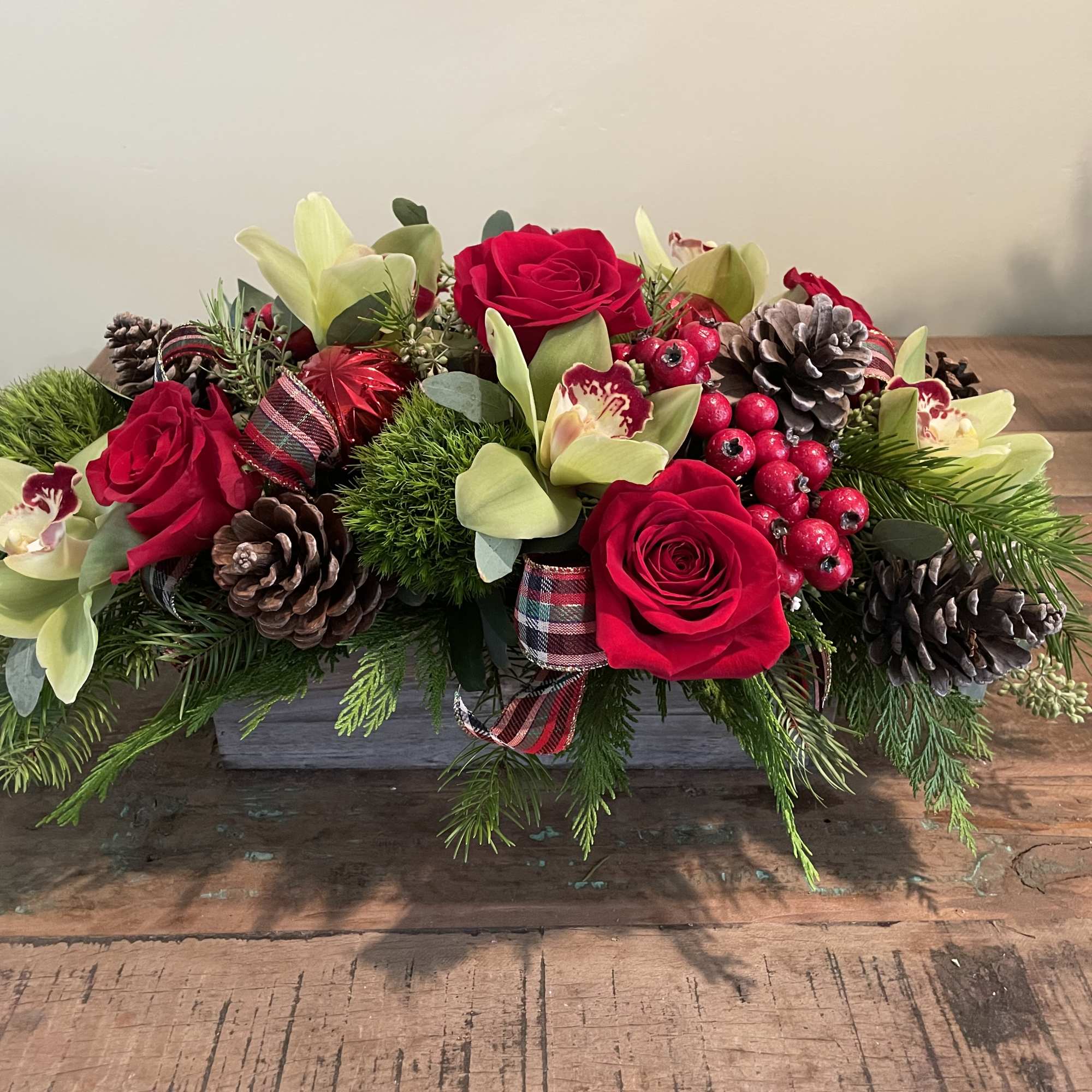 Red roses and pale orchids arranged with pinecones in a low centerpiece