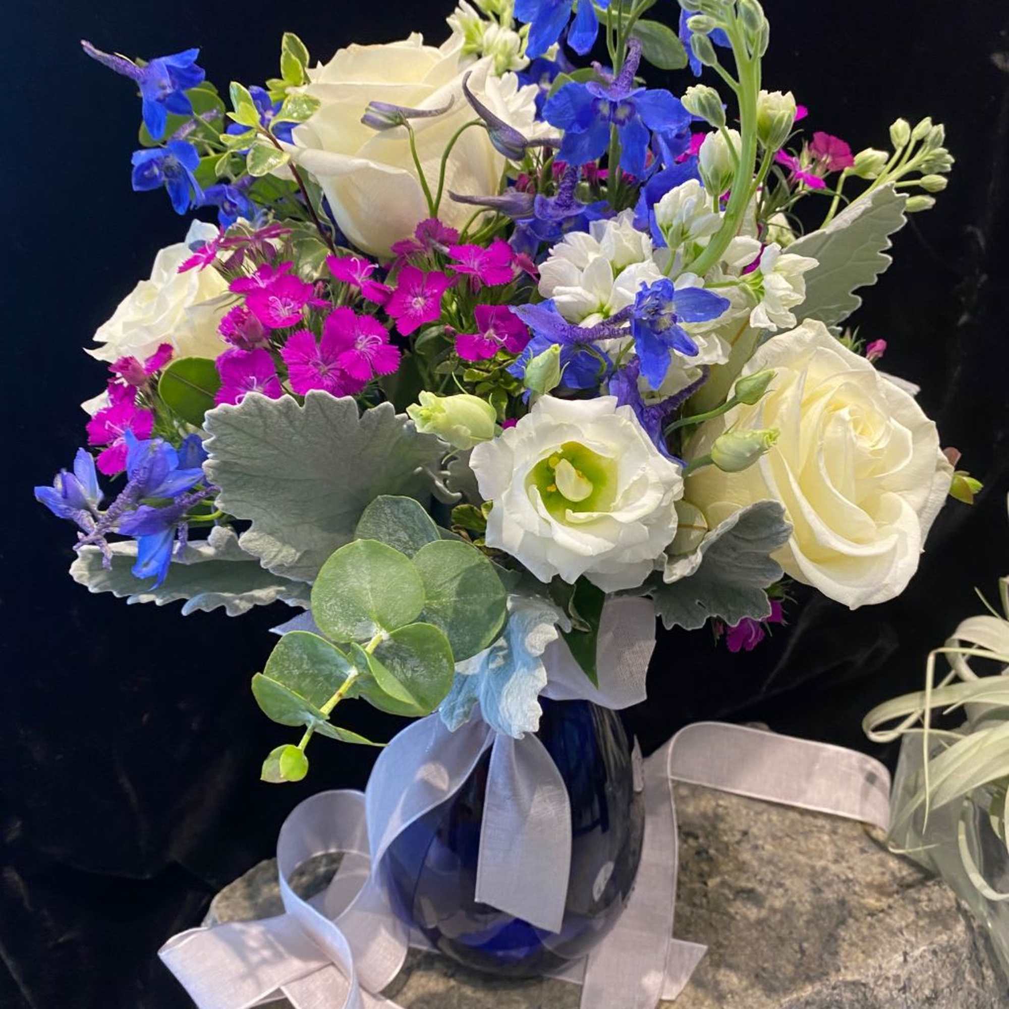 Bouquet of white roses, blue flowers, and pink dianthus in a blue vase