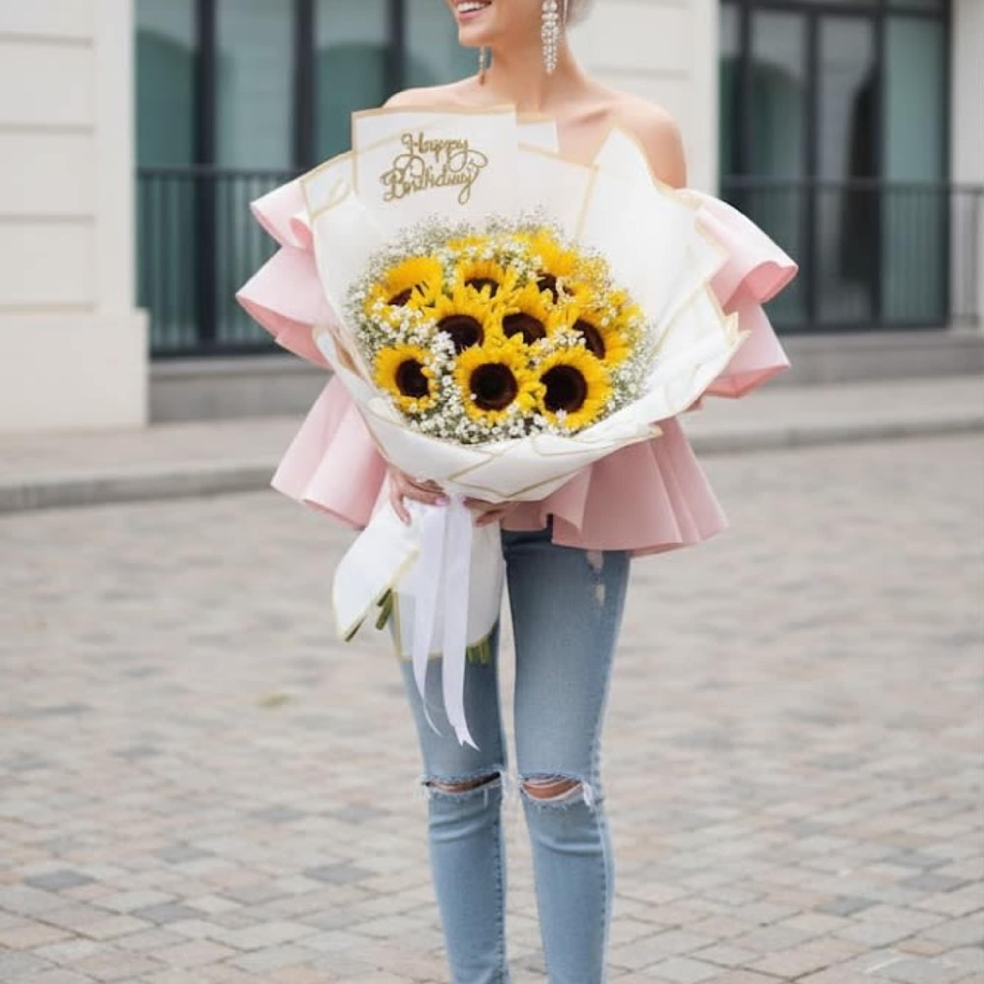 Woman holding a large bouquet of sunflowers wrapped in white and pink paper