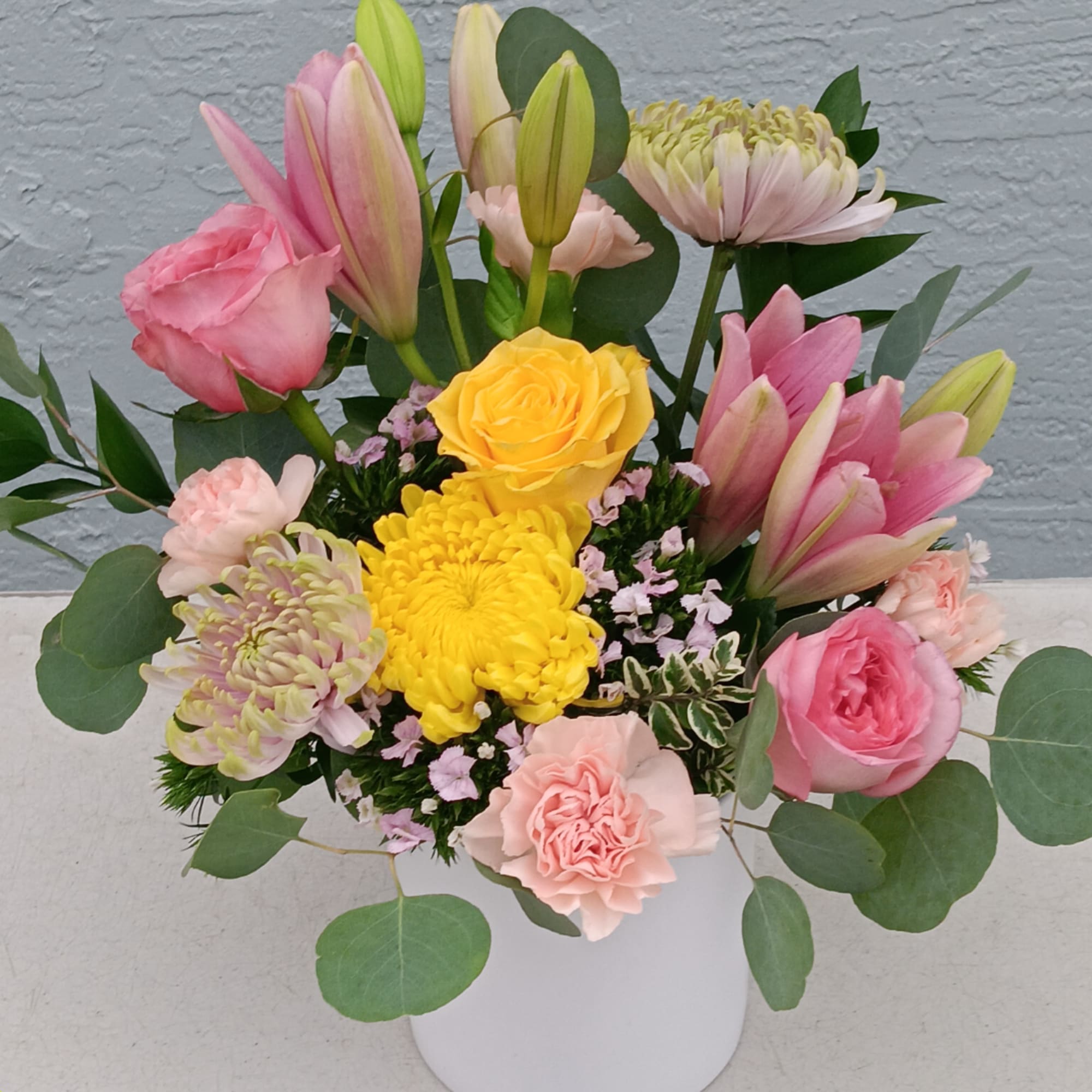 Mixed bouquet of pink lilies, roses, carnations, and yellow chrysanthemums in a white vase