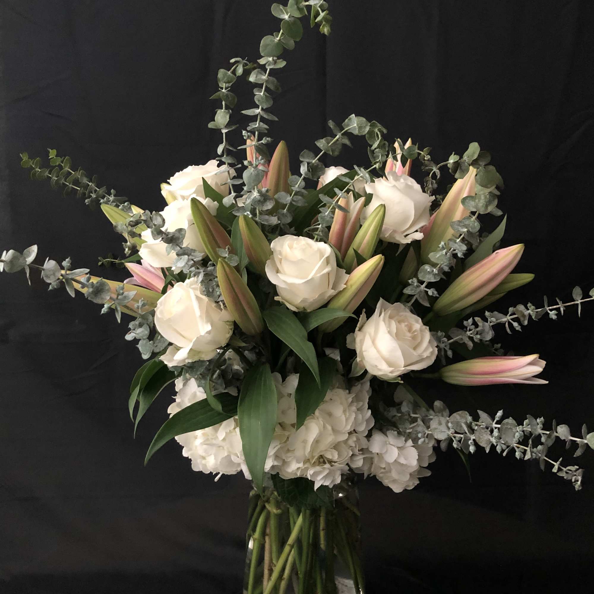 White roses and lilies in a glass vase with trailing eucalyptus