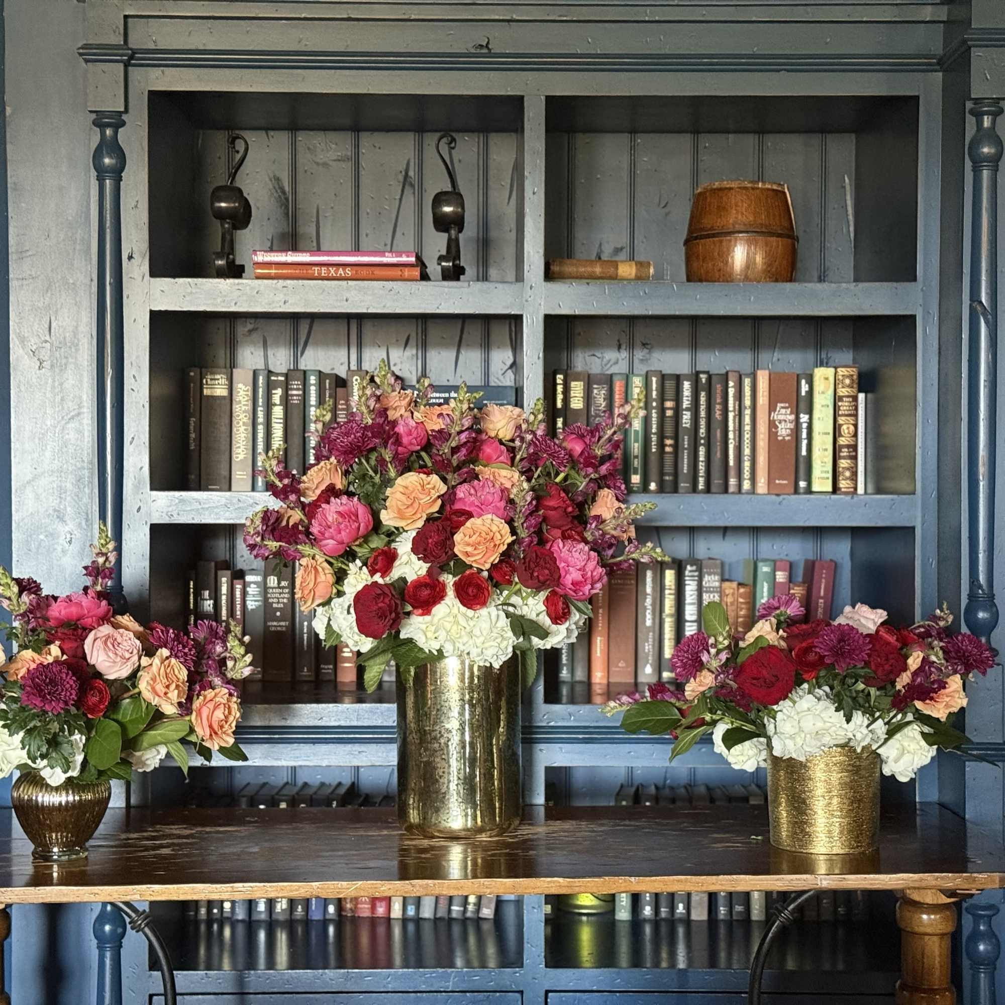 Three floral arrangements in gold vases on a table
