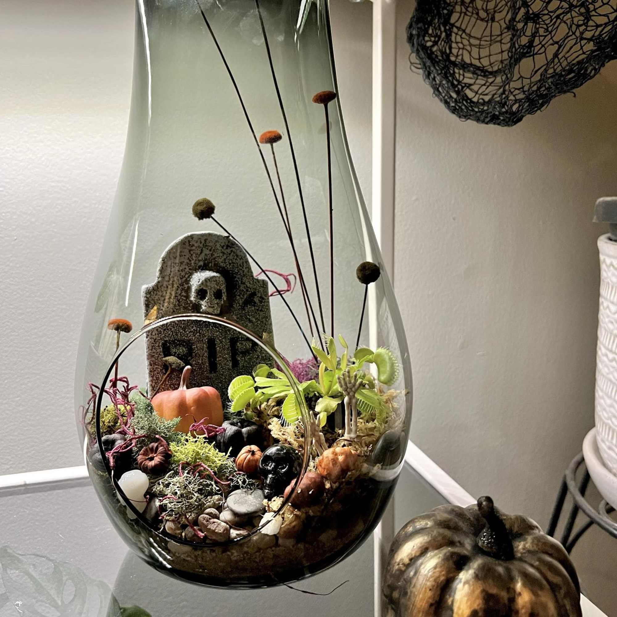 Halloween terrarium in a glass vase with a miniature tombstone and pumpkins