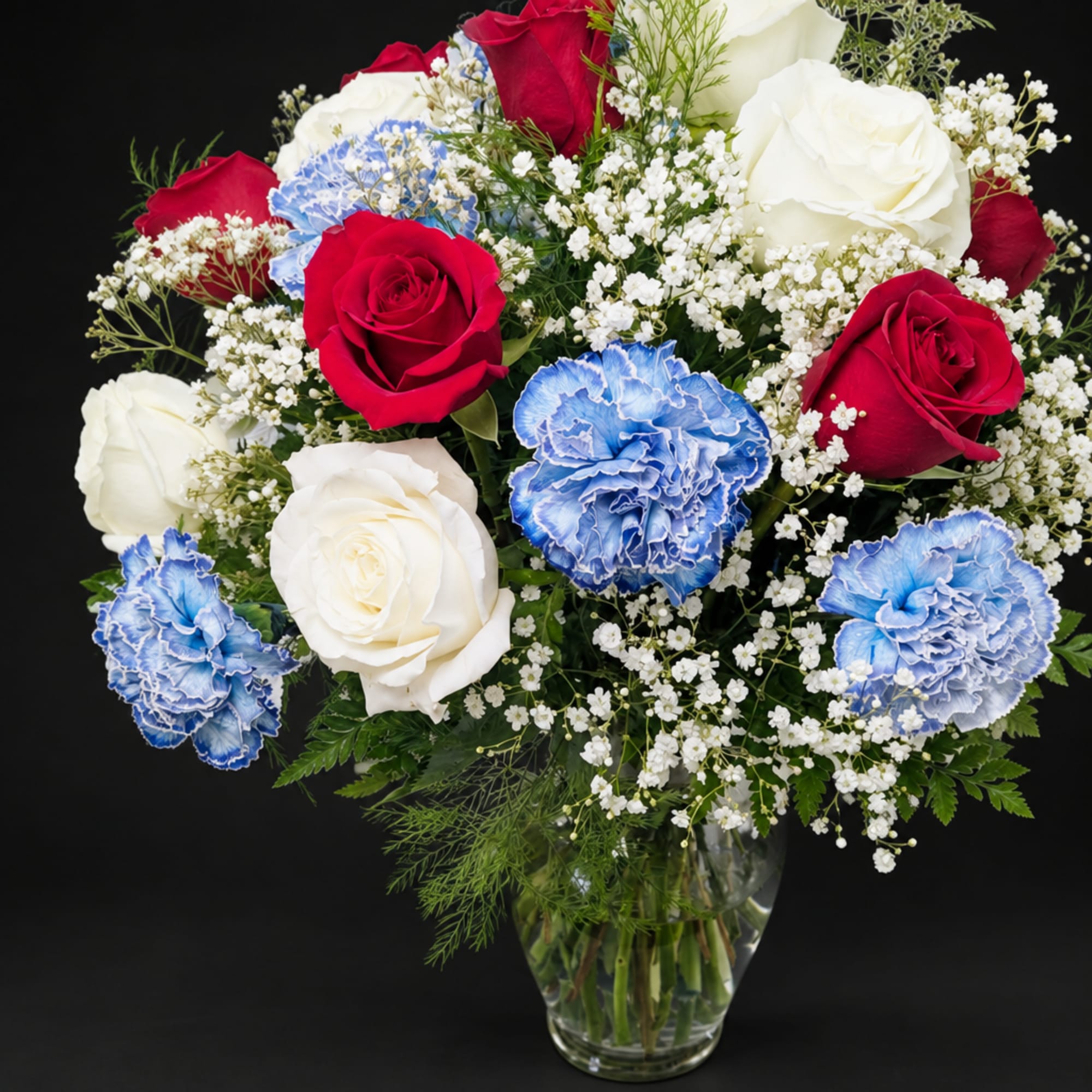 Bouquet of red and white roses with blue carnations in a glass vase