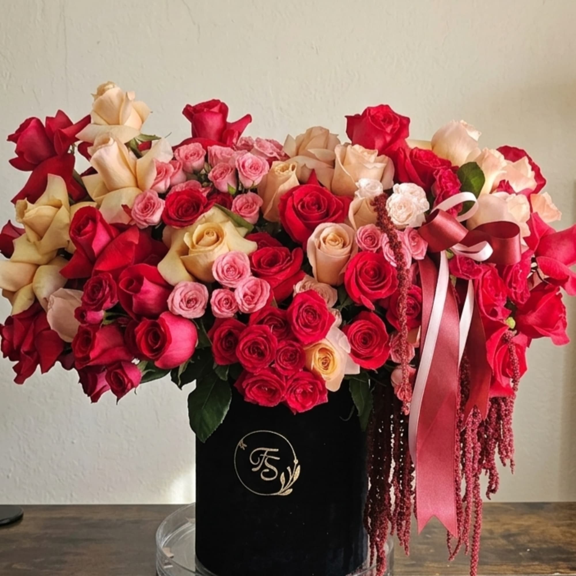 Large bouquet of red, pink, and cream roses in a black box with ribbon