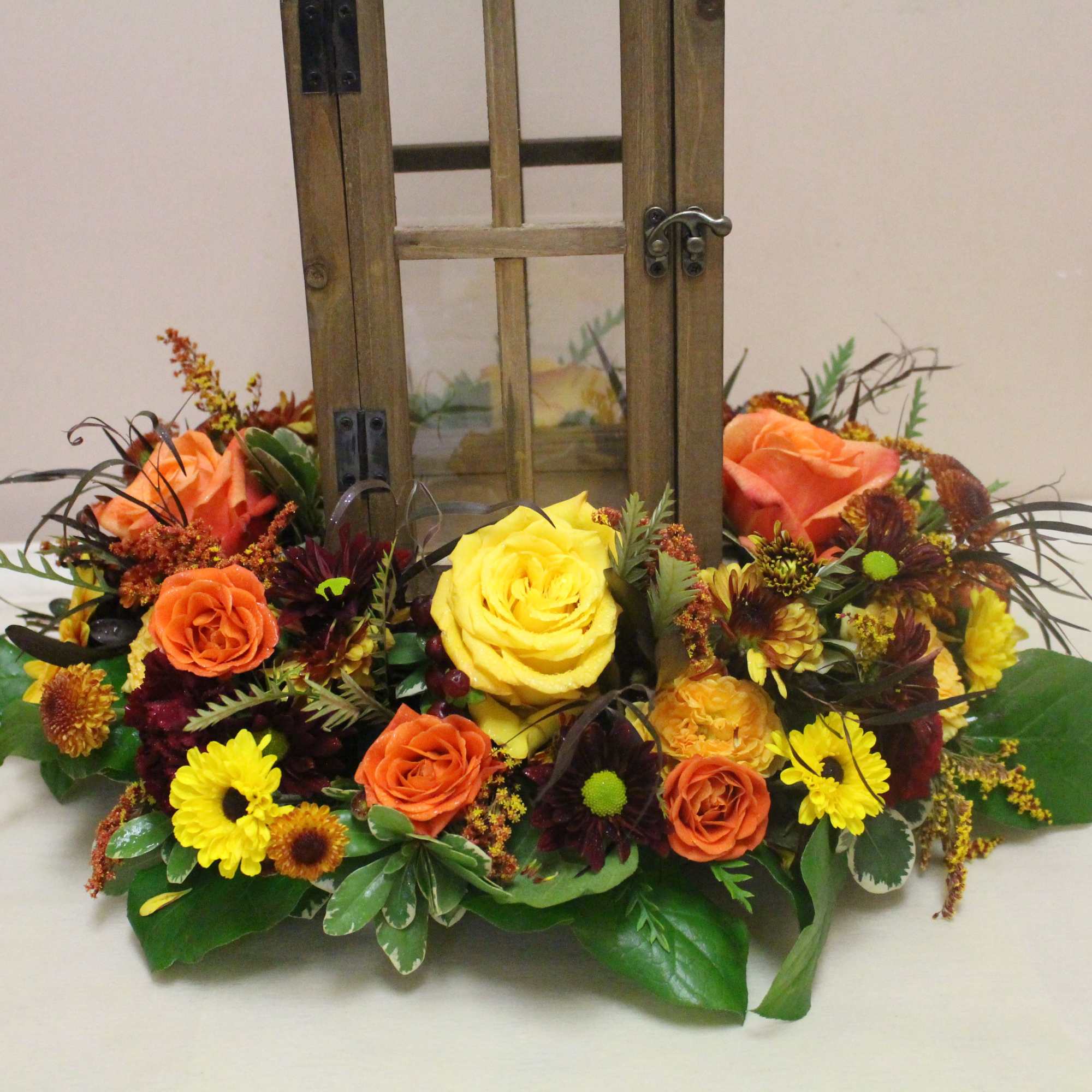 Low floral arrangement with yellow and orange roses and small yellow daisies in a wooden lantern