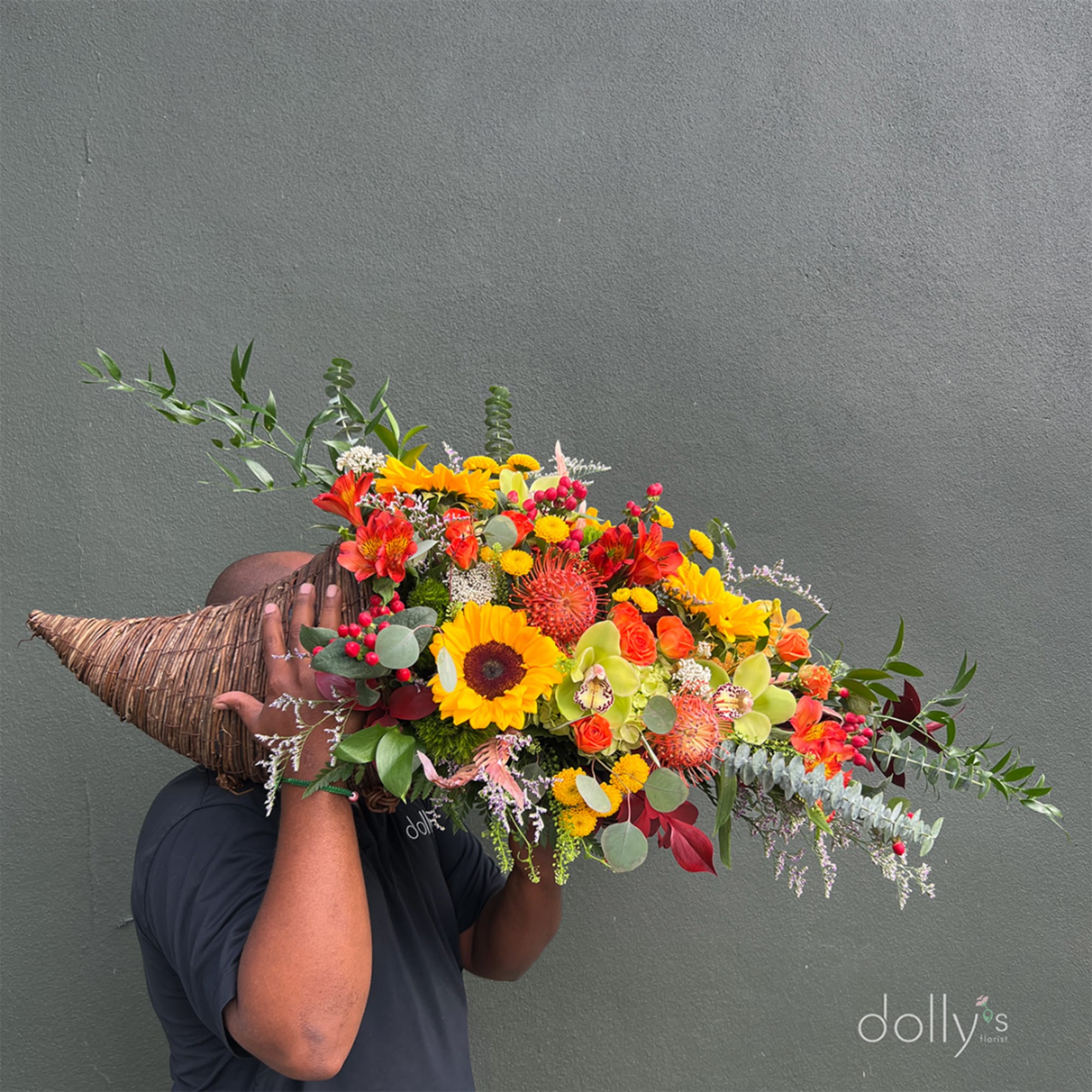 Large mixed bouquet with sunflowers, orange blooms, and greenery in a woven wrap