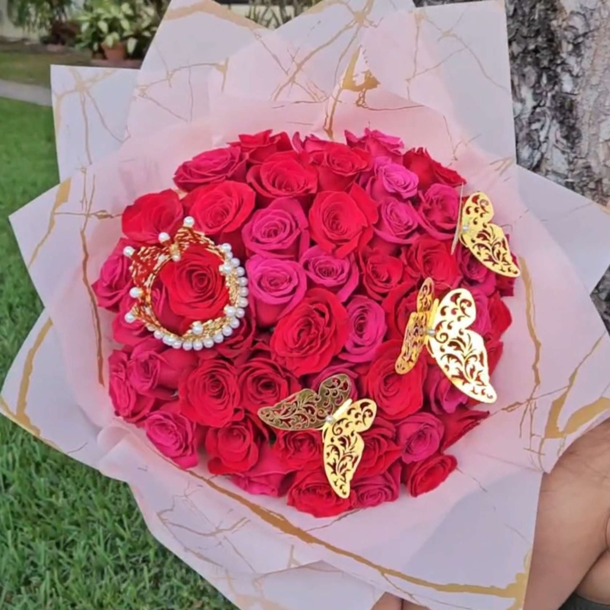 Bouquet of red roses wrapped in pink paper with gold butterfly accents