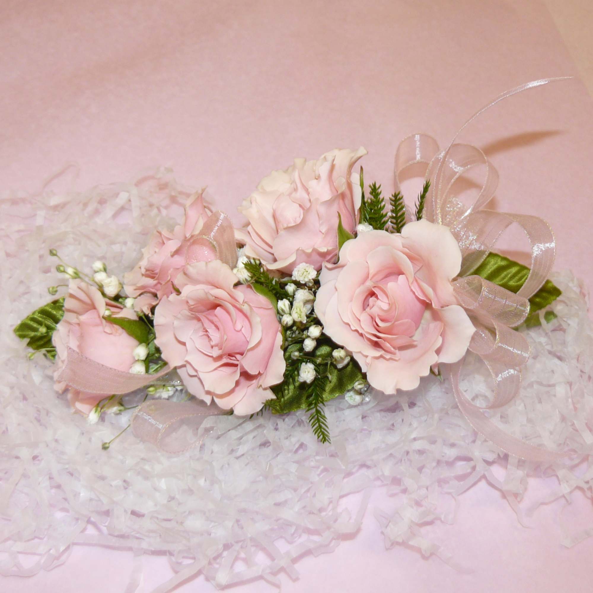Pink rose corsage with ribbon on pale shredded paper