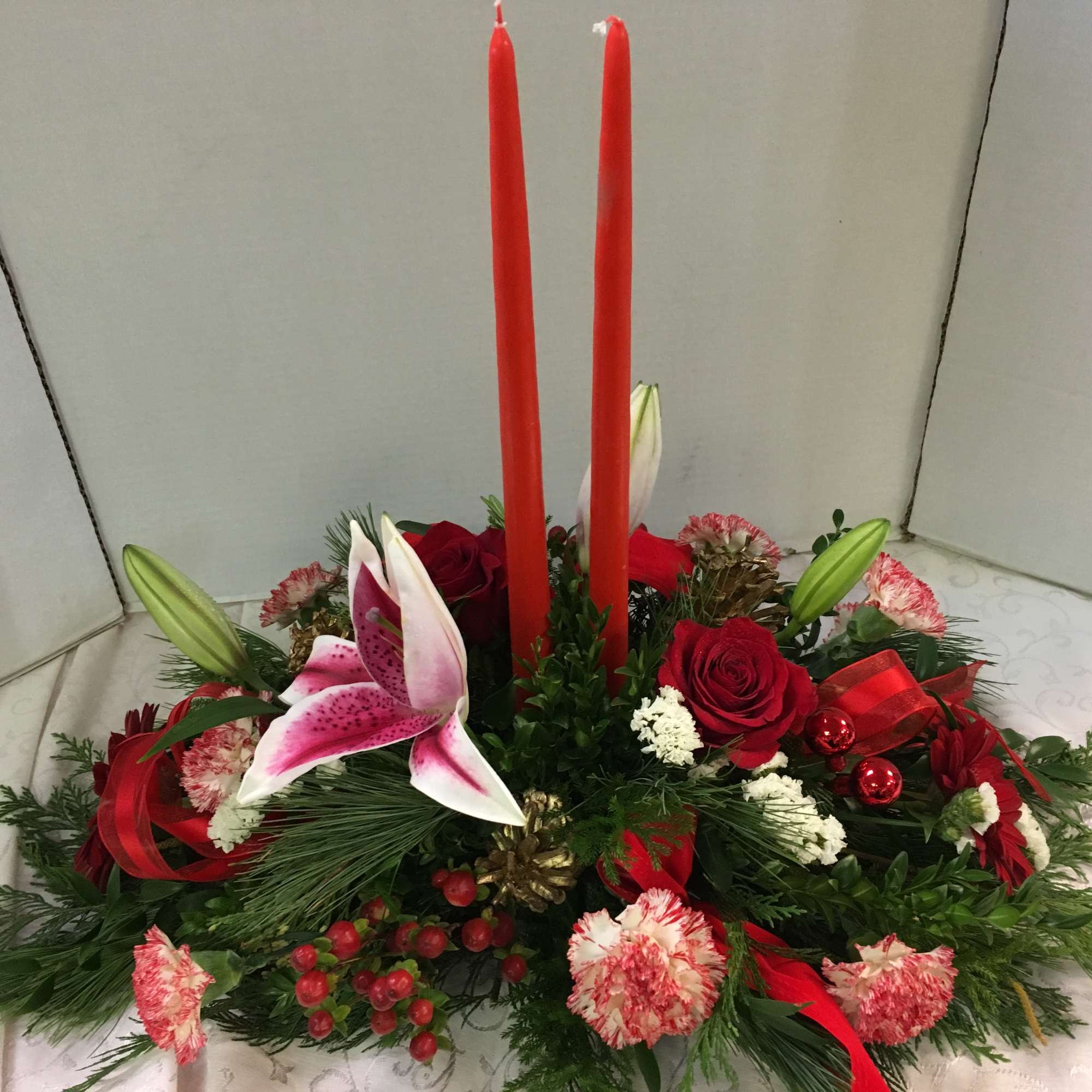 Low floral centerpiece with red candles, roses, and pink lilies