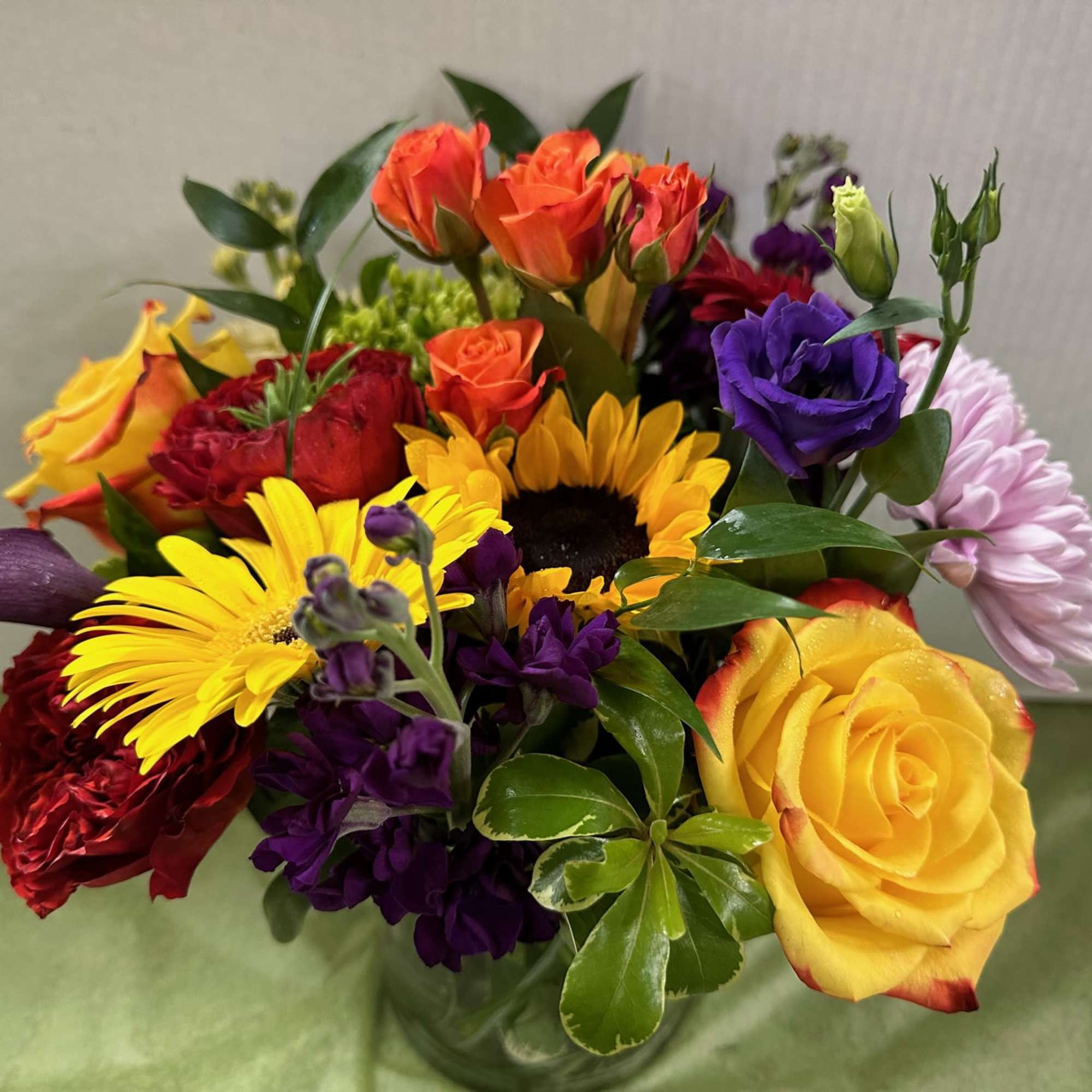 Mixed bouquet of roses, sunflowers, and purple blooms in a glass vase
