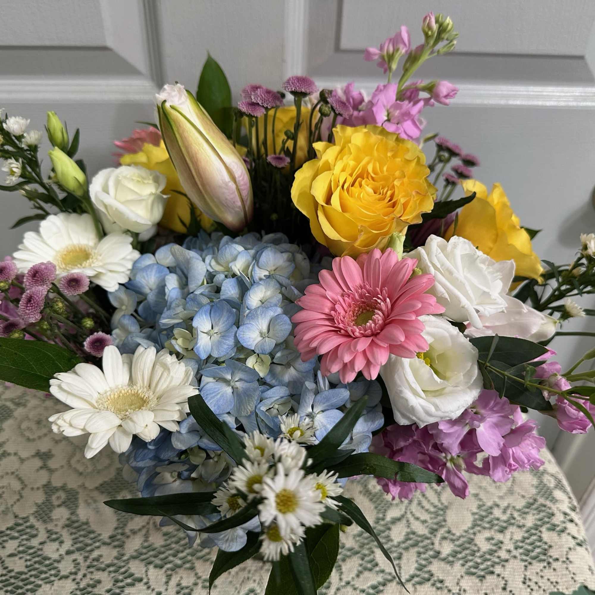 Mixed bouquet with blue hydrangea, yellow and white roses, pink gerbera daisies, and lilies