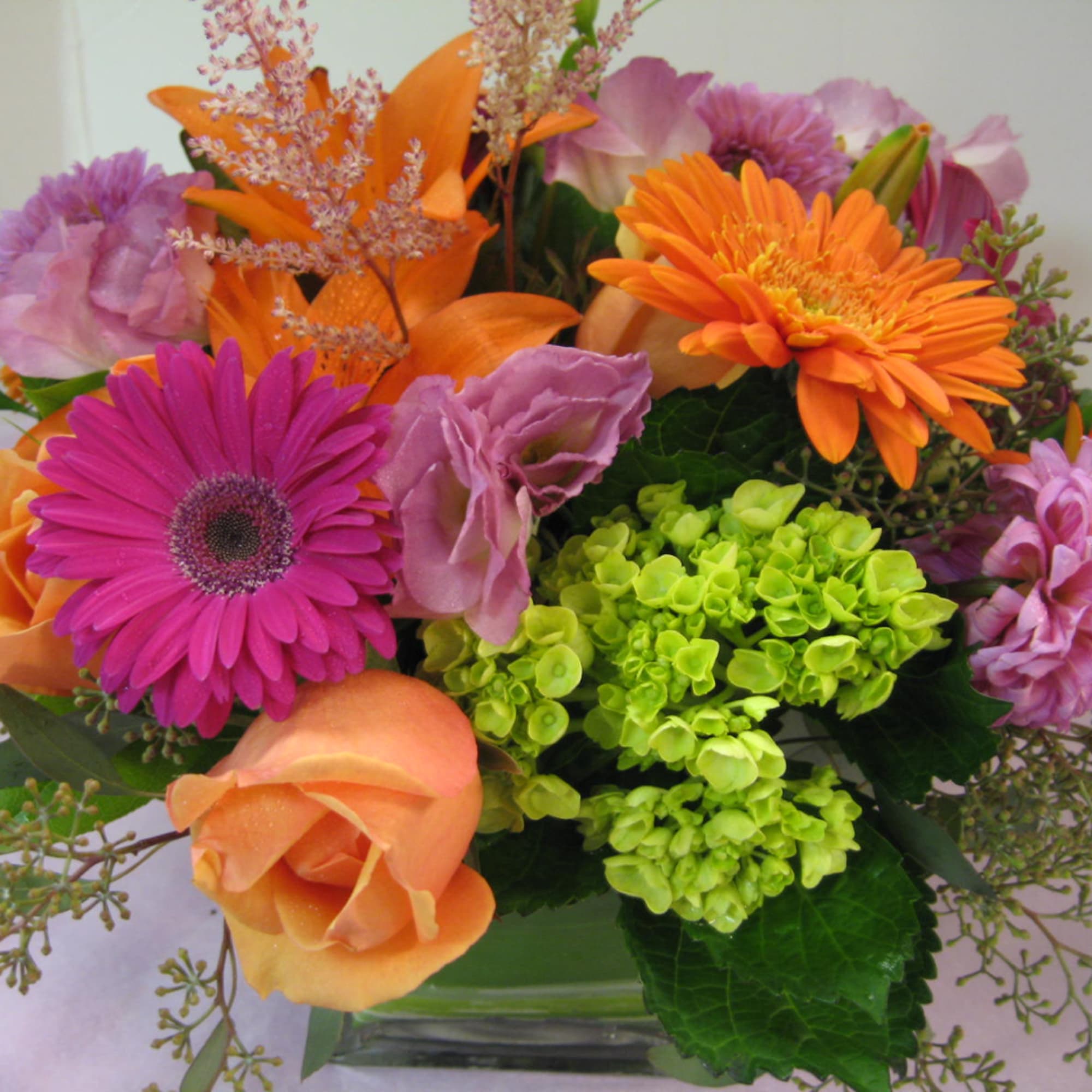 Mixed bouquet with orange, pink, and purple flowers in a glass vase