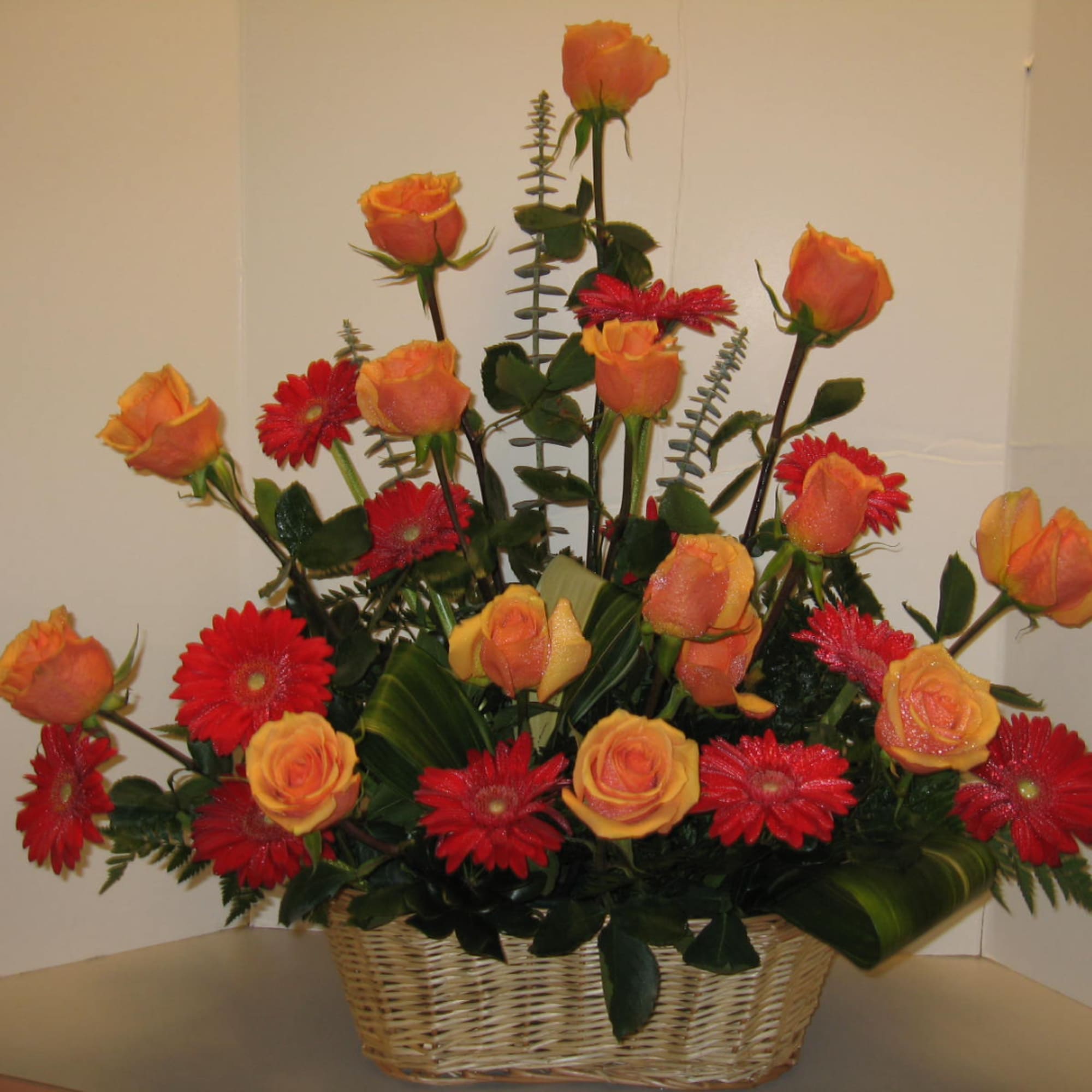 Basket arrangement of orange roses and red daisies