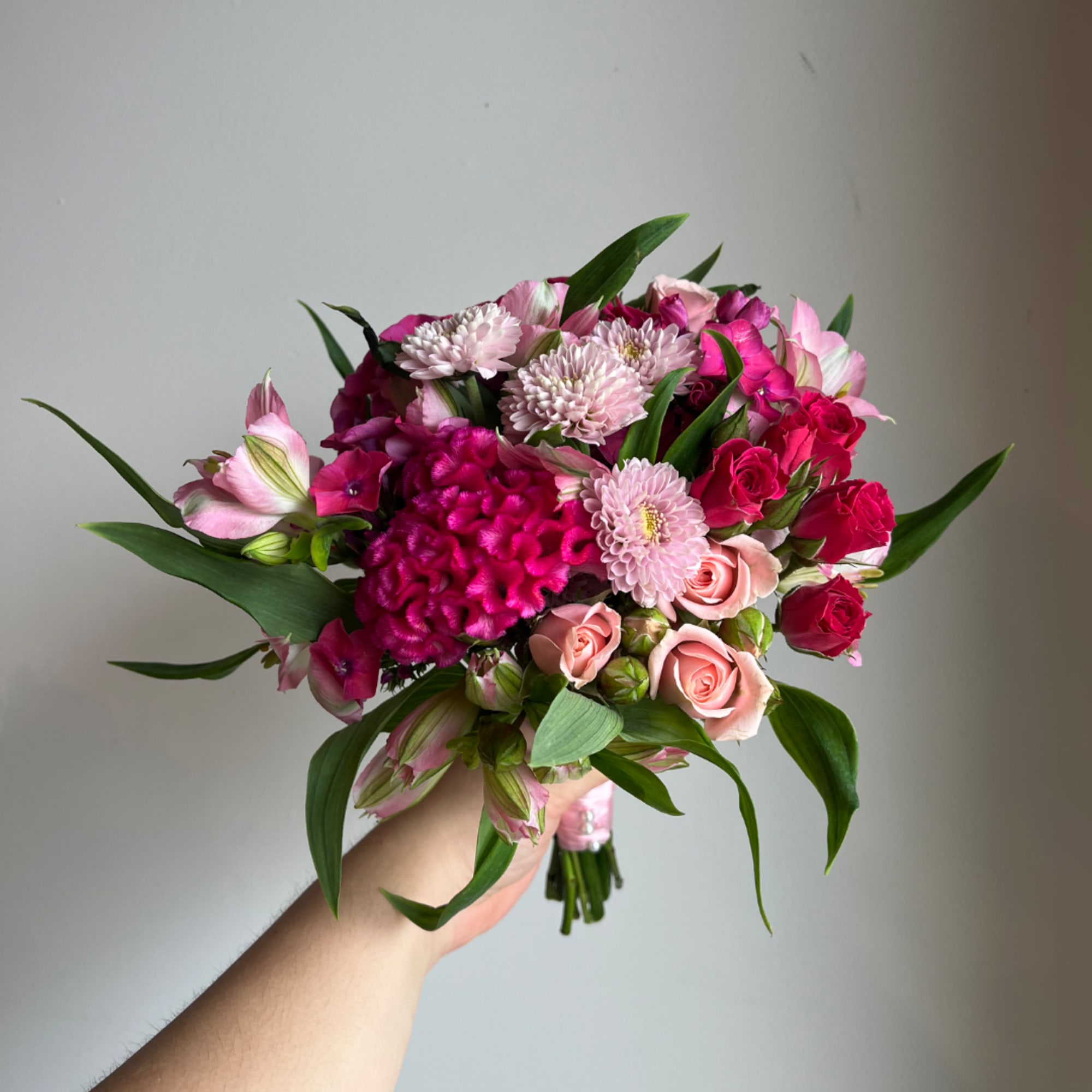 Handheld bouquet of pink and magenta flowers with roses and daisies