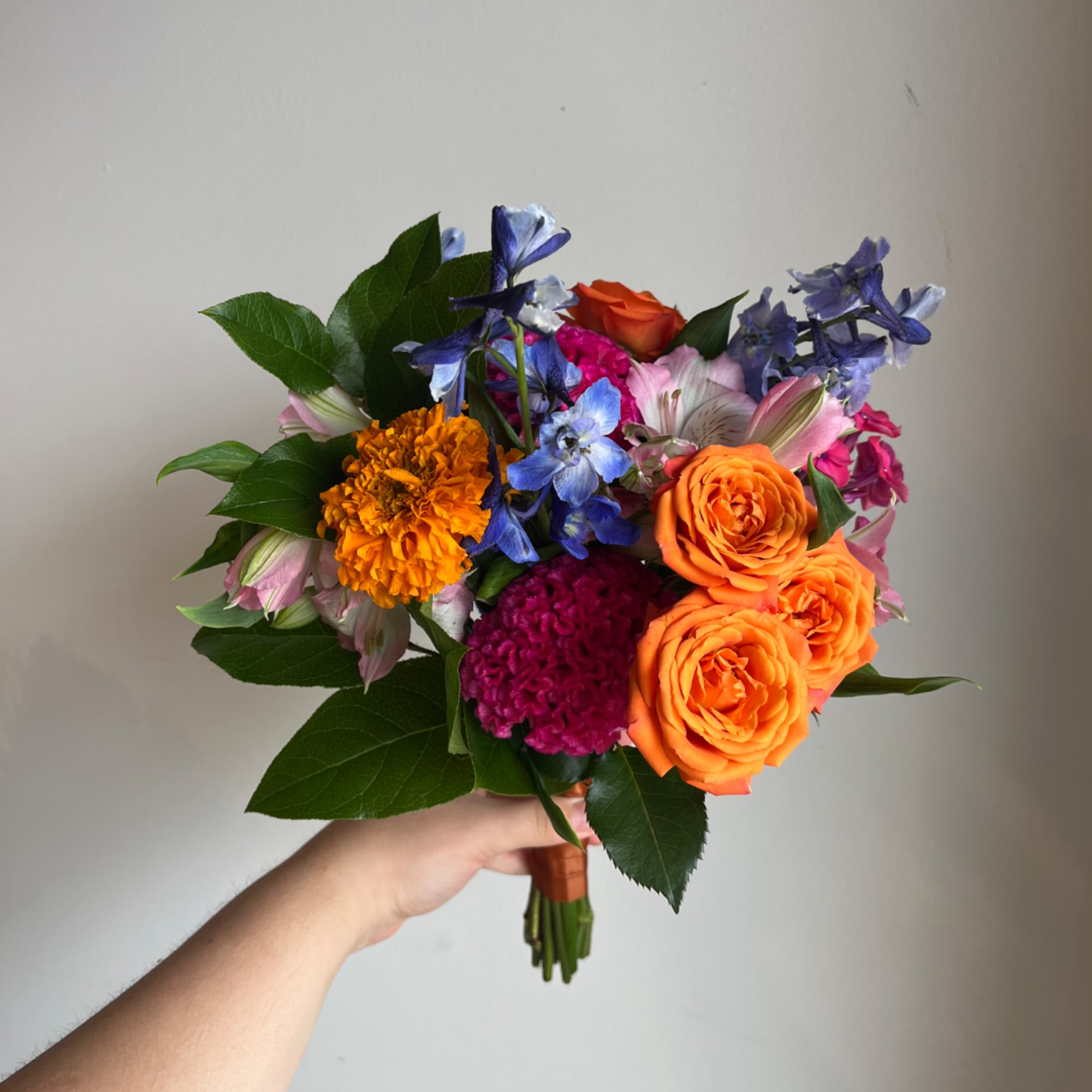 Handheld bouquet with orange roses, blue flowers, and pink blooms