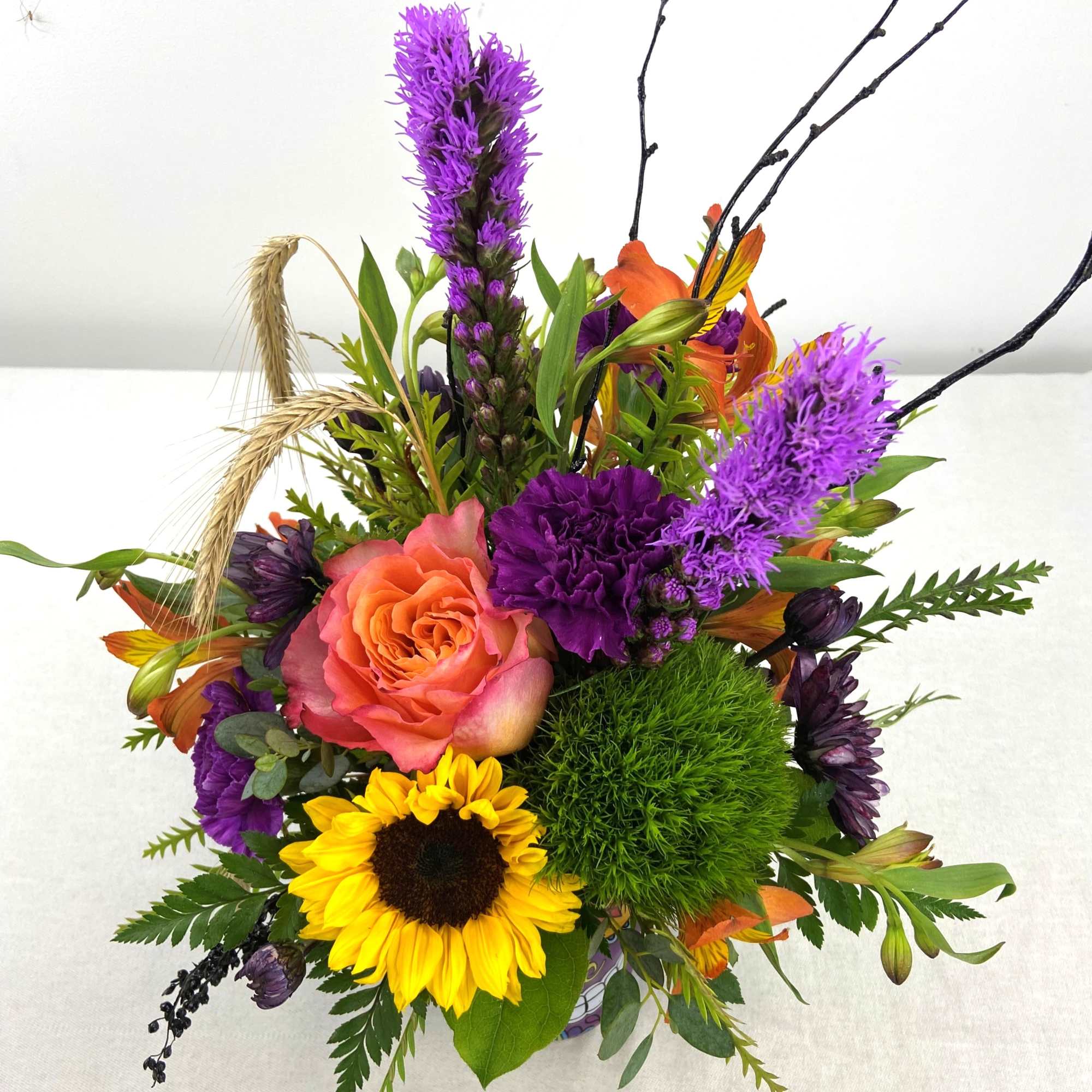 Mixed bouquet with a peach rose, sunflower, purple blooms, and green accents
