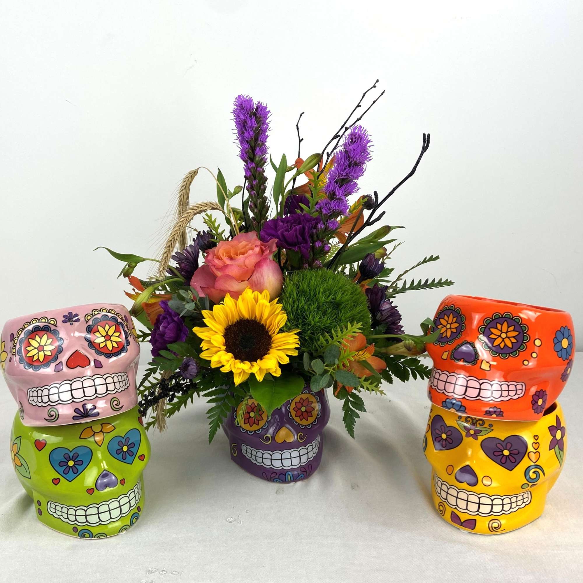 Colorful floral arrangement in a purple sugar skull vase with three decorative skull planters nearby