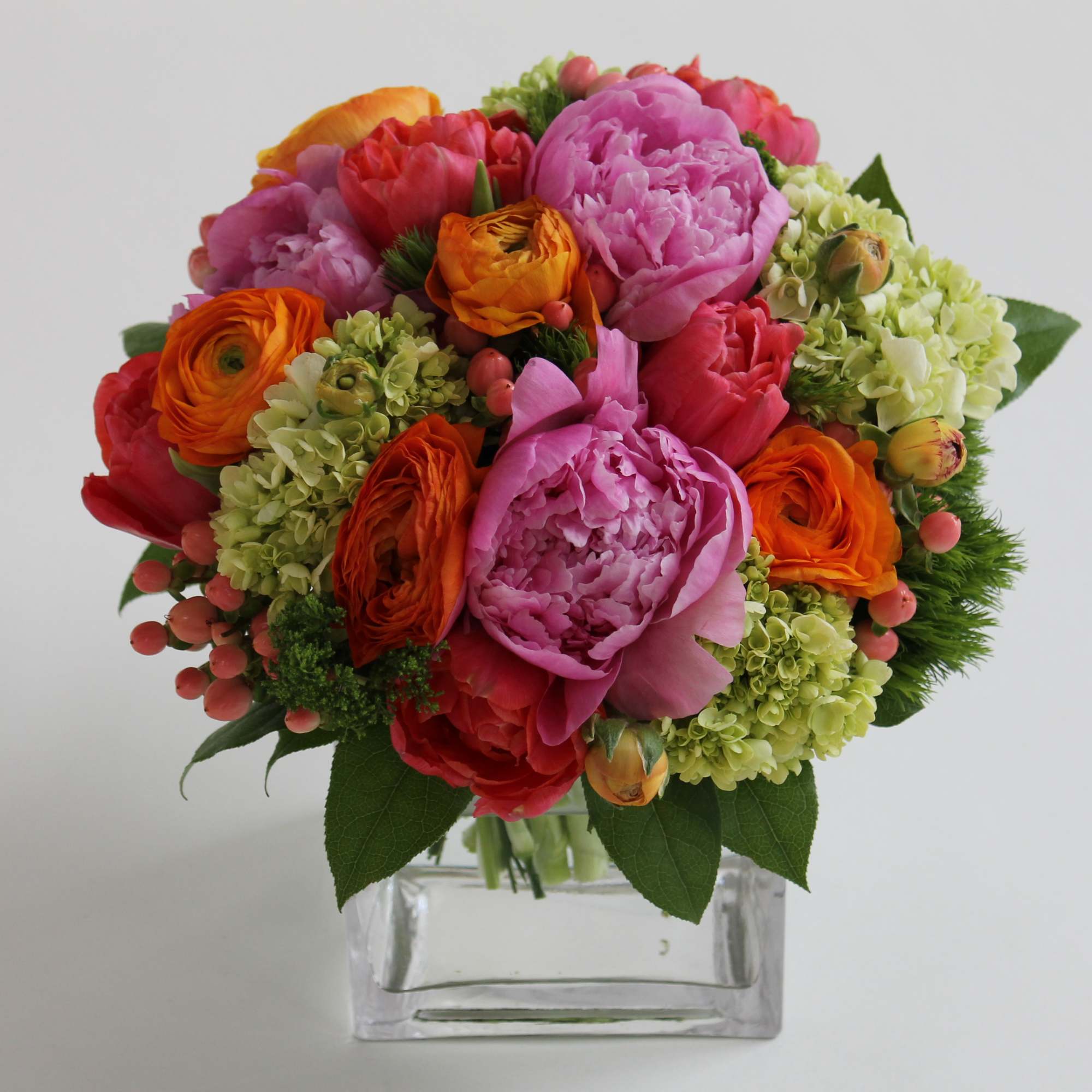 Colorful bouquet of pink, orange, and red flowers in a clear square vase