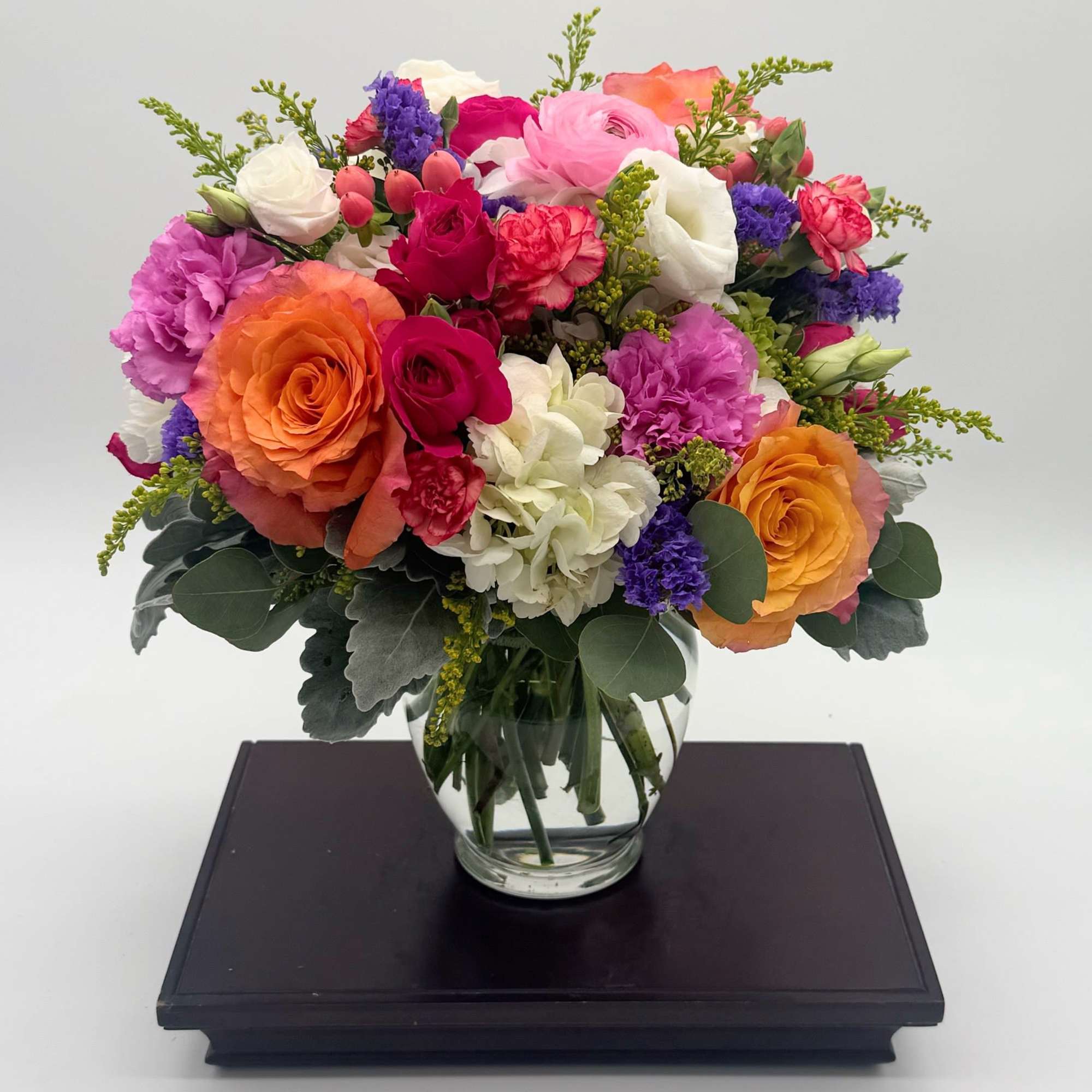 Bright mixed bouquet of roses, carnations, and hydrangeas in a round clear glass vase