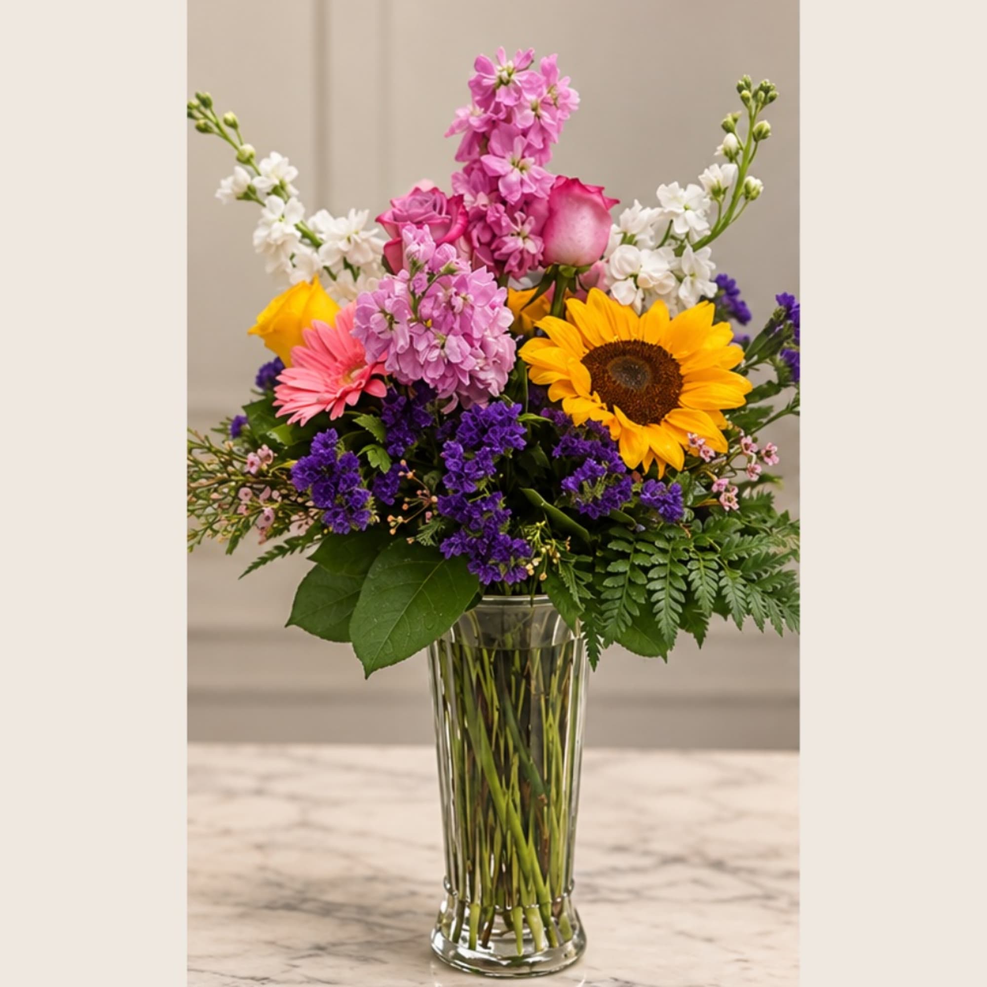Mixed bouquet with sunflowers, pink roses, and purple flowers in a glass vase