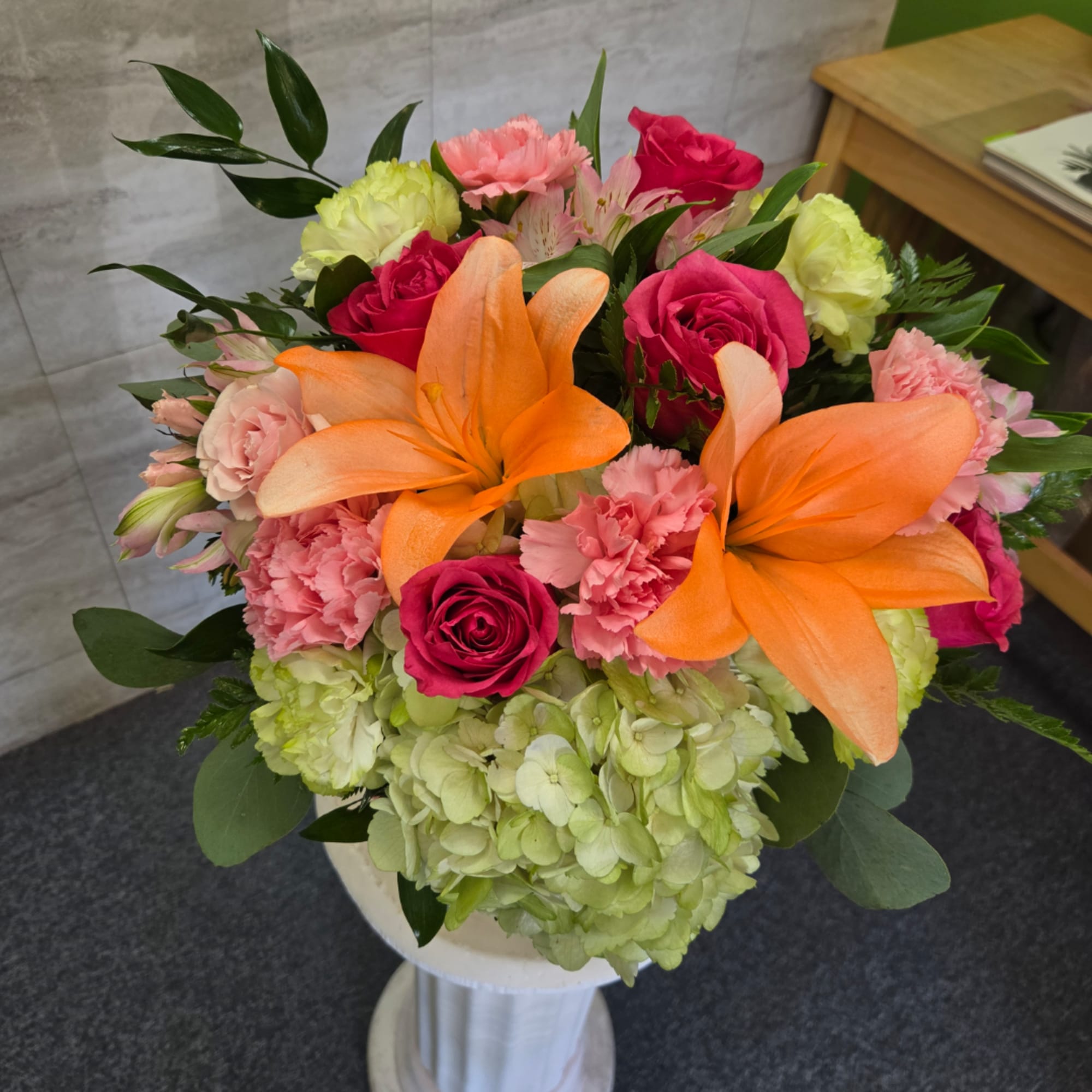 Bouquet of orange lilies, pink roses, carnations, and green hydrangeas in a white vase