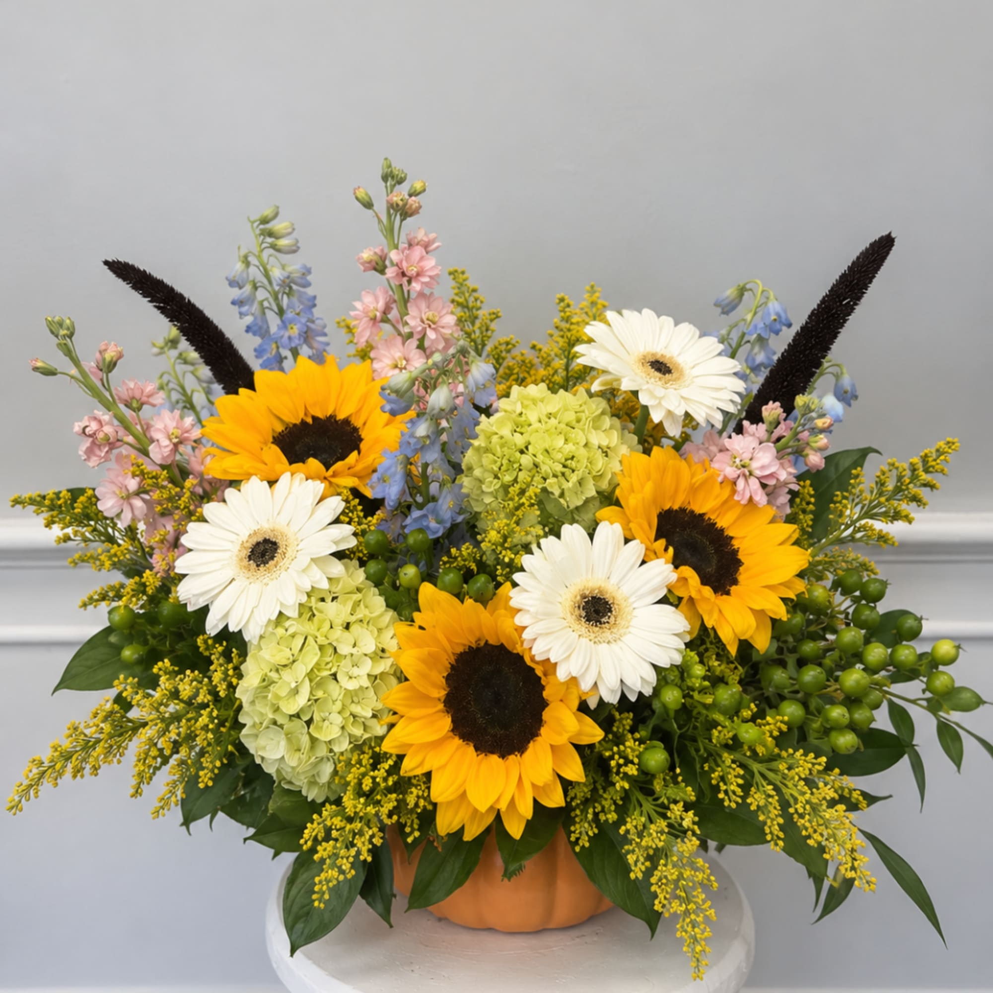 Mixed bouquet with sunflowers, white gerbera daisies, and pastel blooms in a pumpkin vase