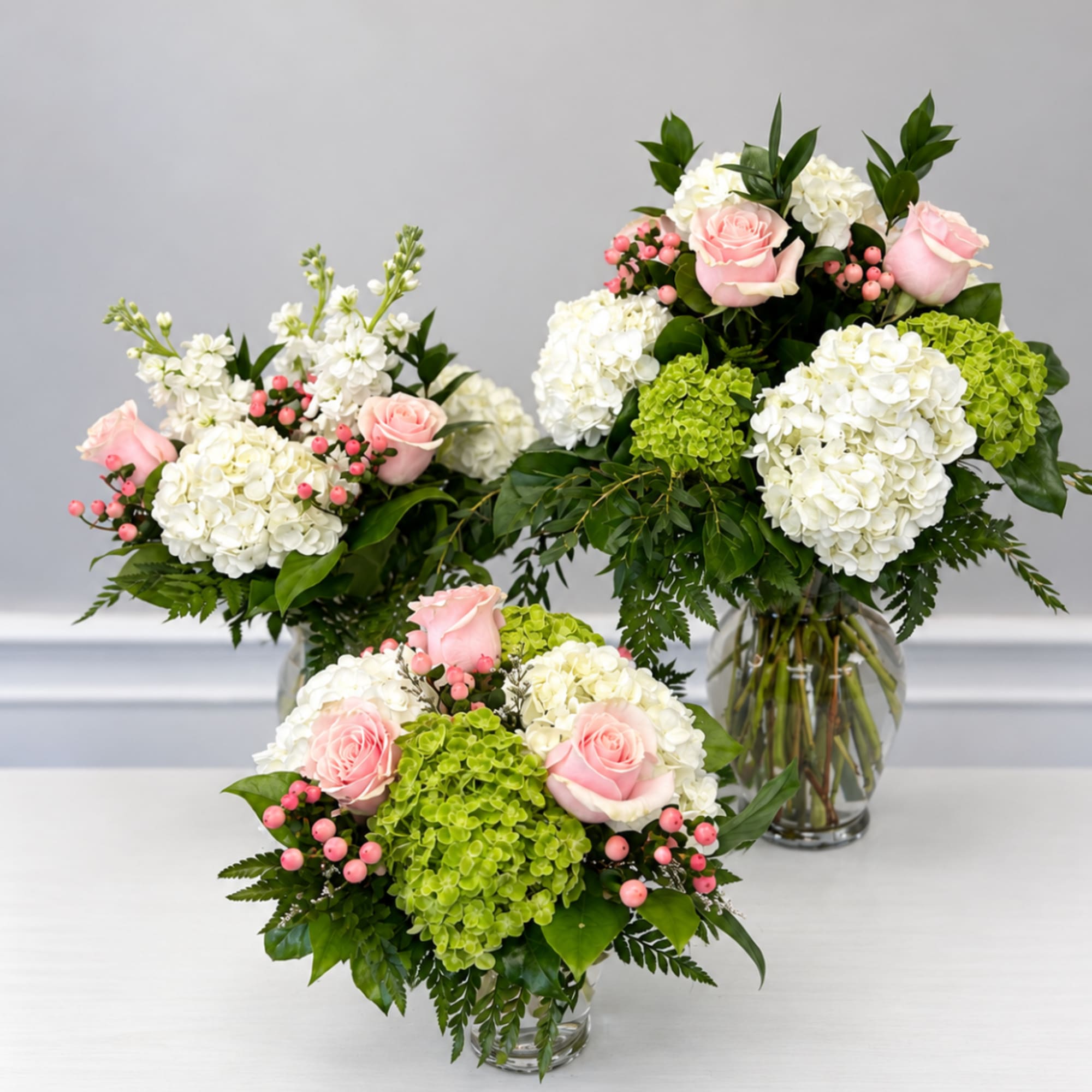 Three pink rose and hydrangea arrangements in clear glass vases