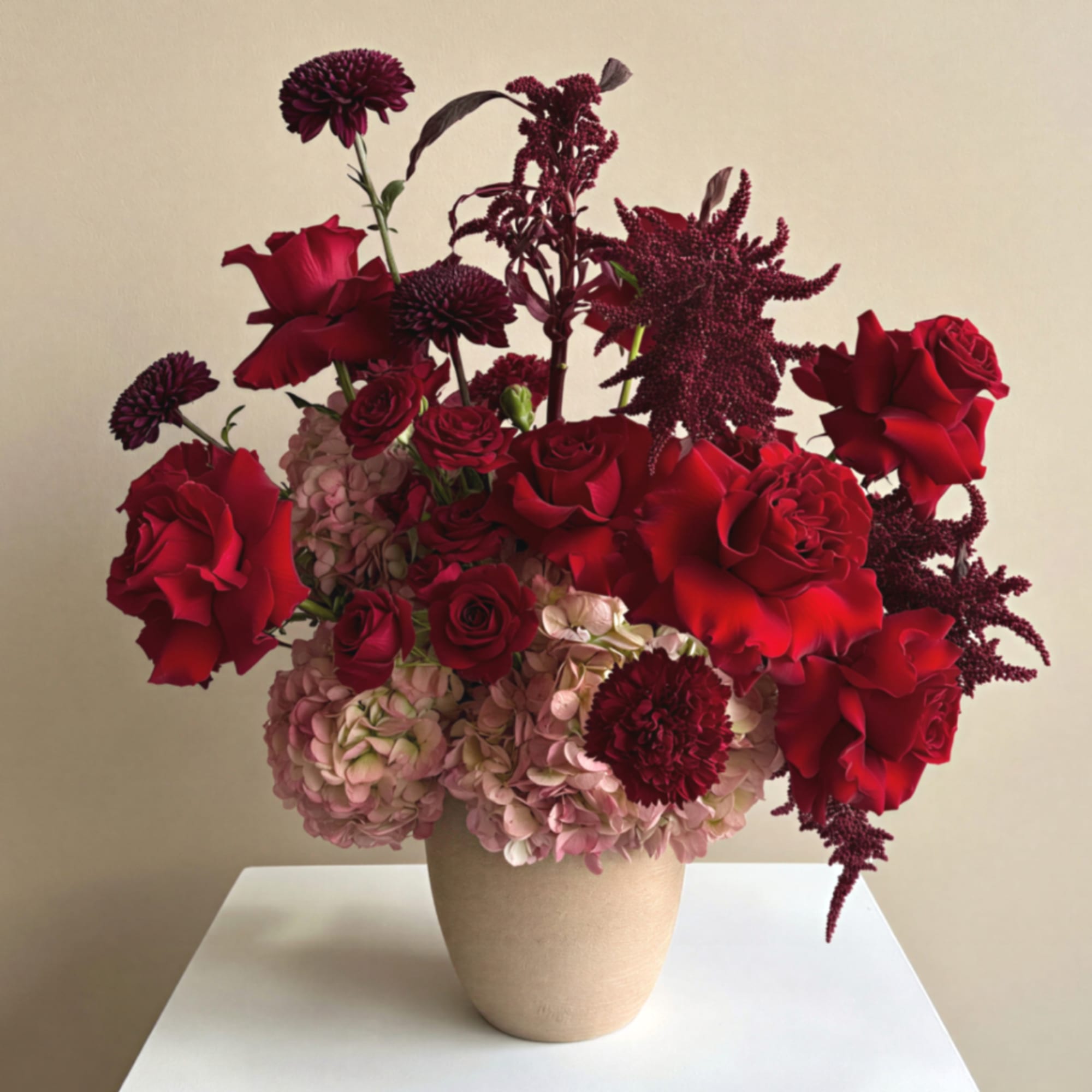 Red roses and burgundy flowers arranged in a beige vase