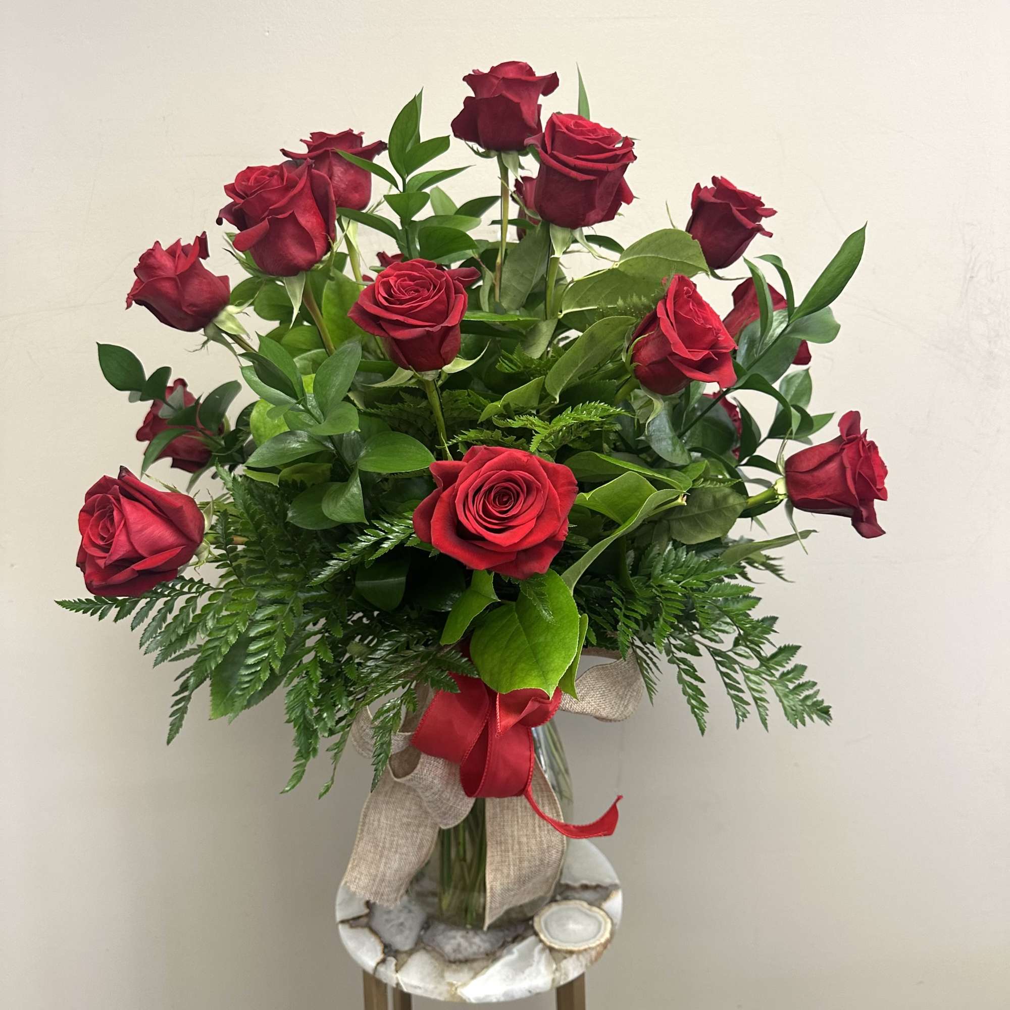 A dozen long stem red roses with assorted greenery in a clear
