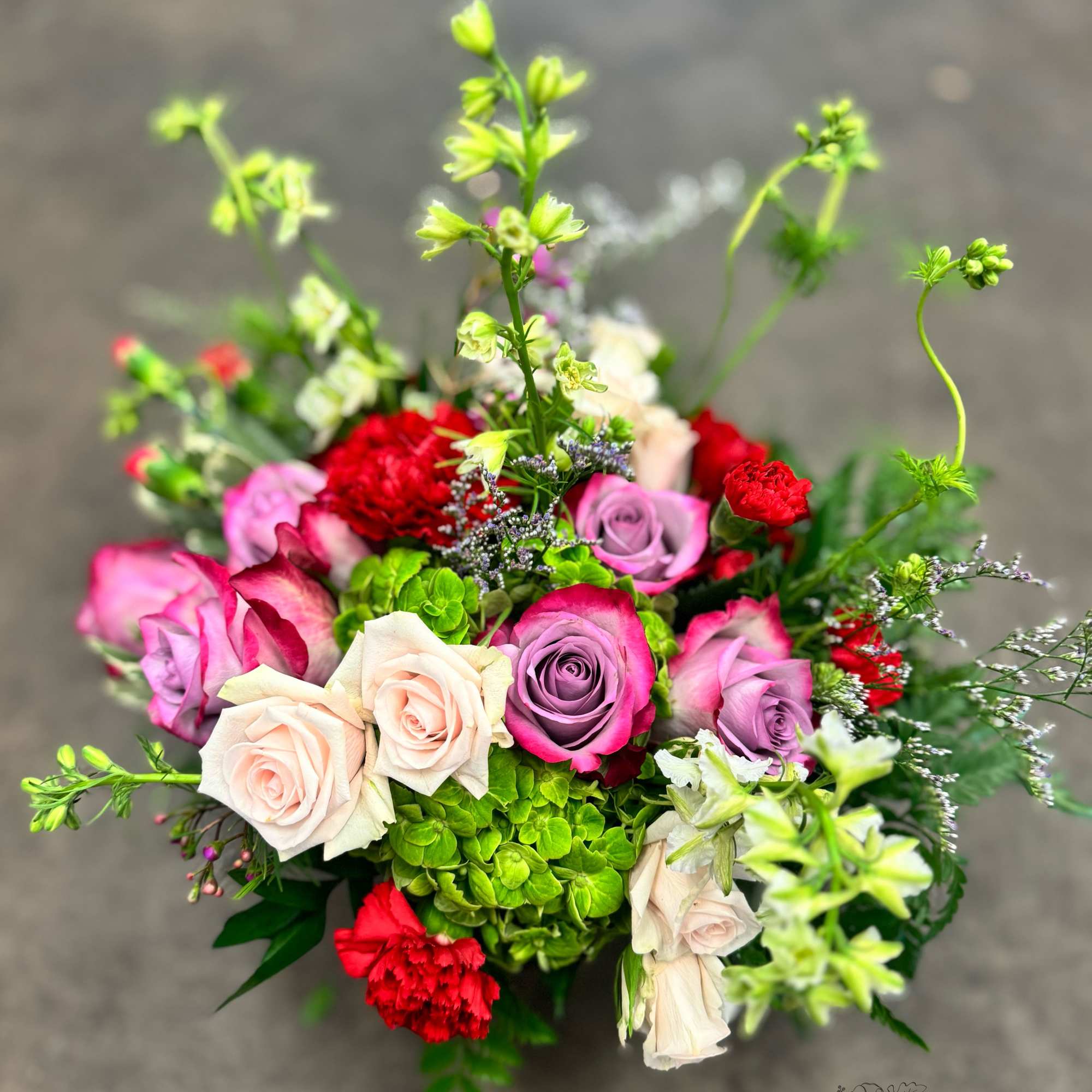 A lush blend of lavender roses, rich red carnations, green hydrangea, blush