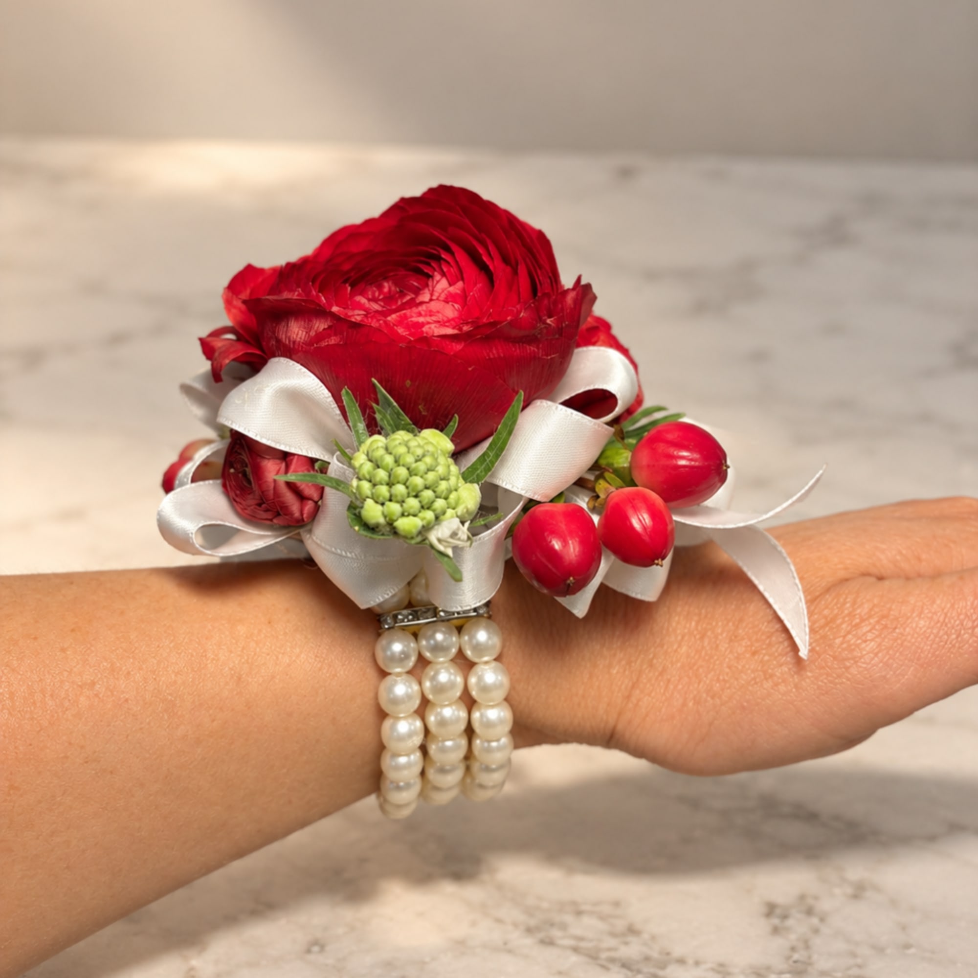 Red floral wrist corsage with white ribbon and pearl bracelet