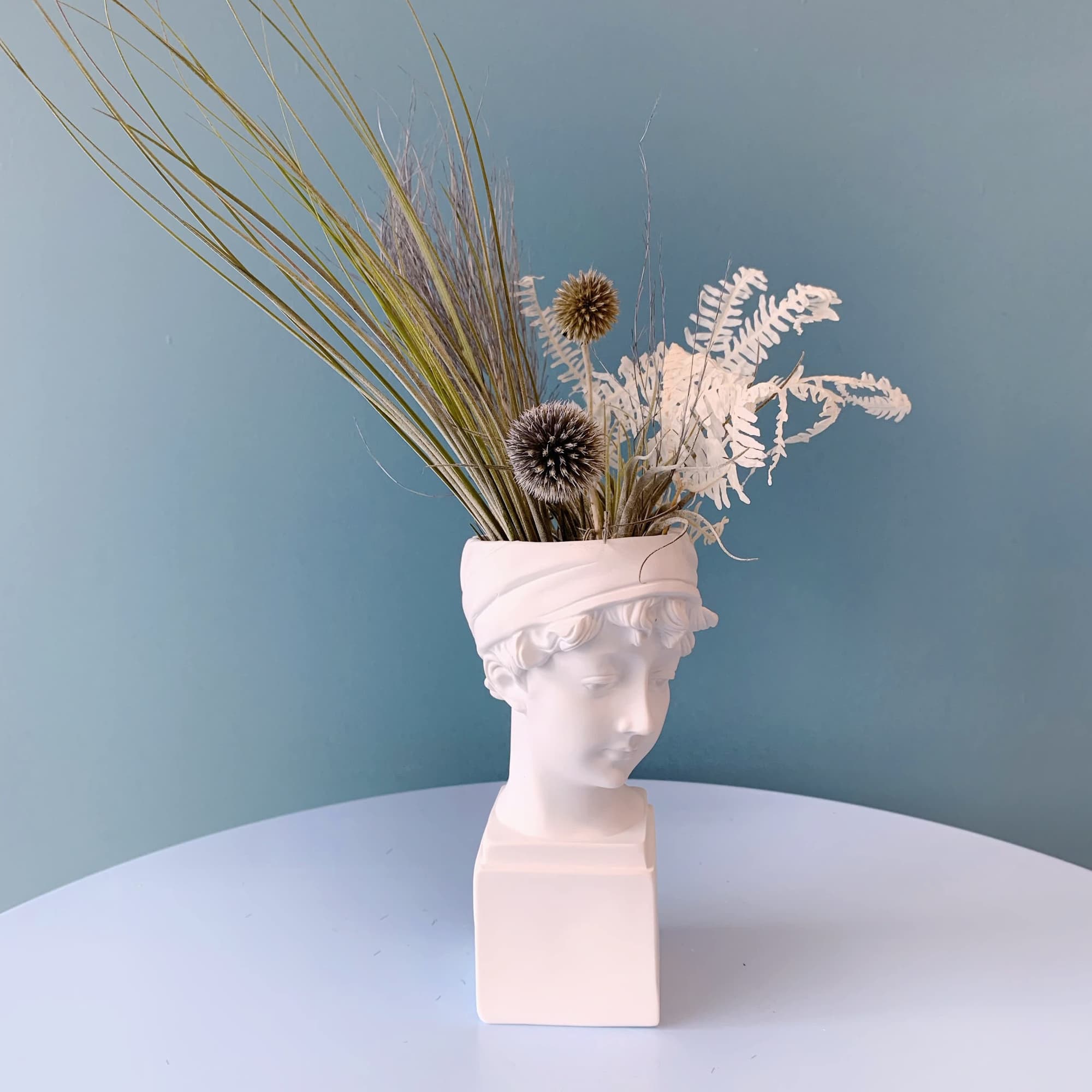 Dried grass arrangement in a white bust vase with spiky seed heads