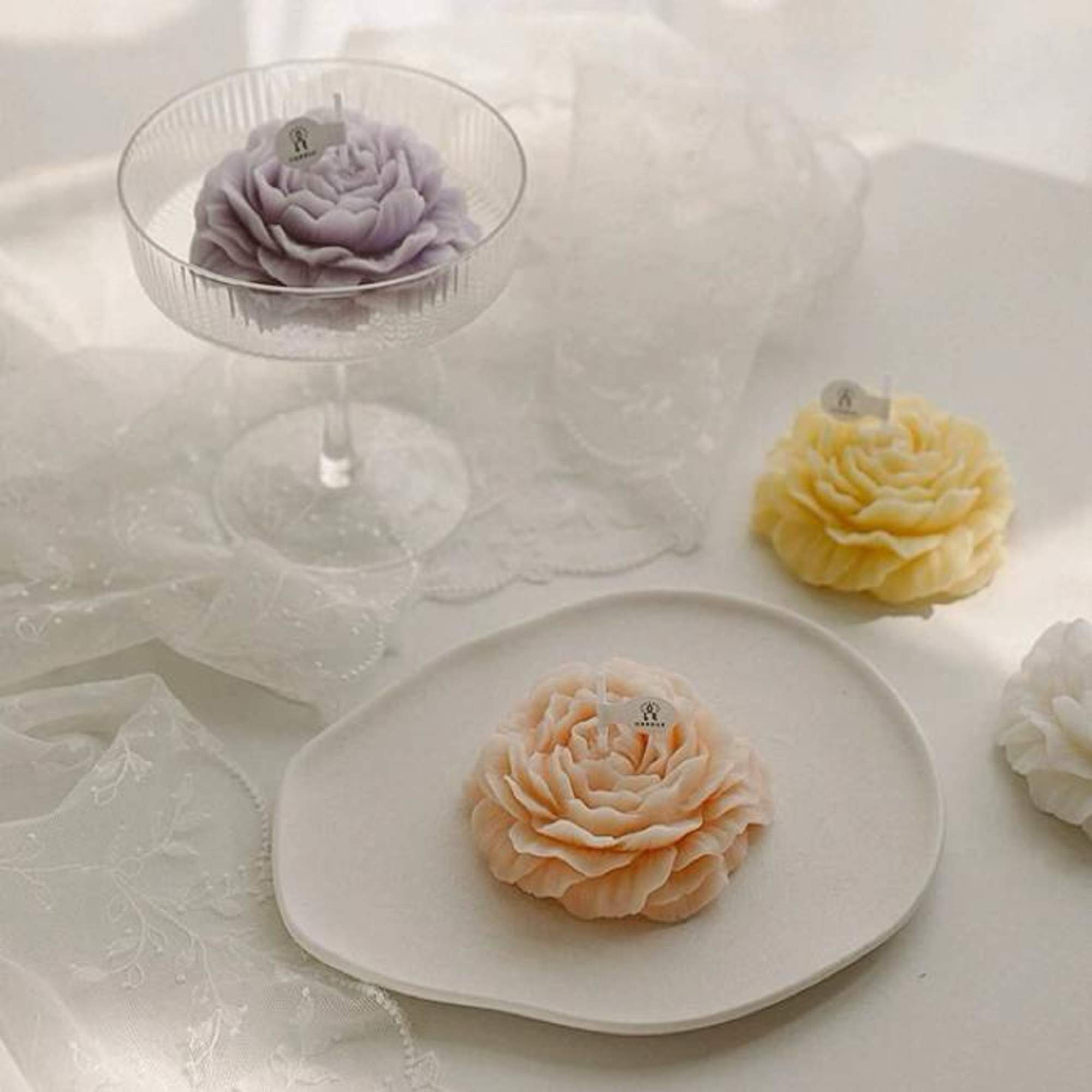 Decorative flower-shaped candles in pastel colors on plates and a glass stand.