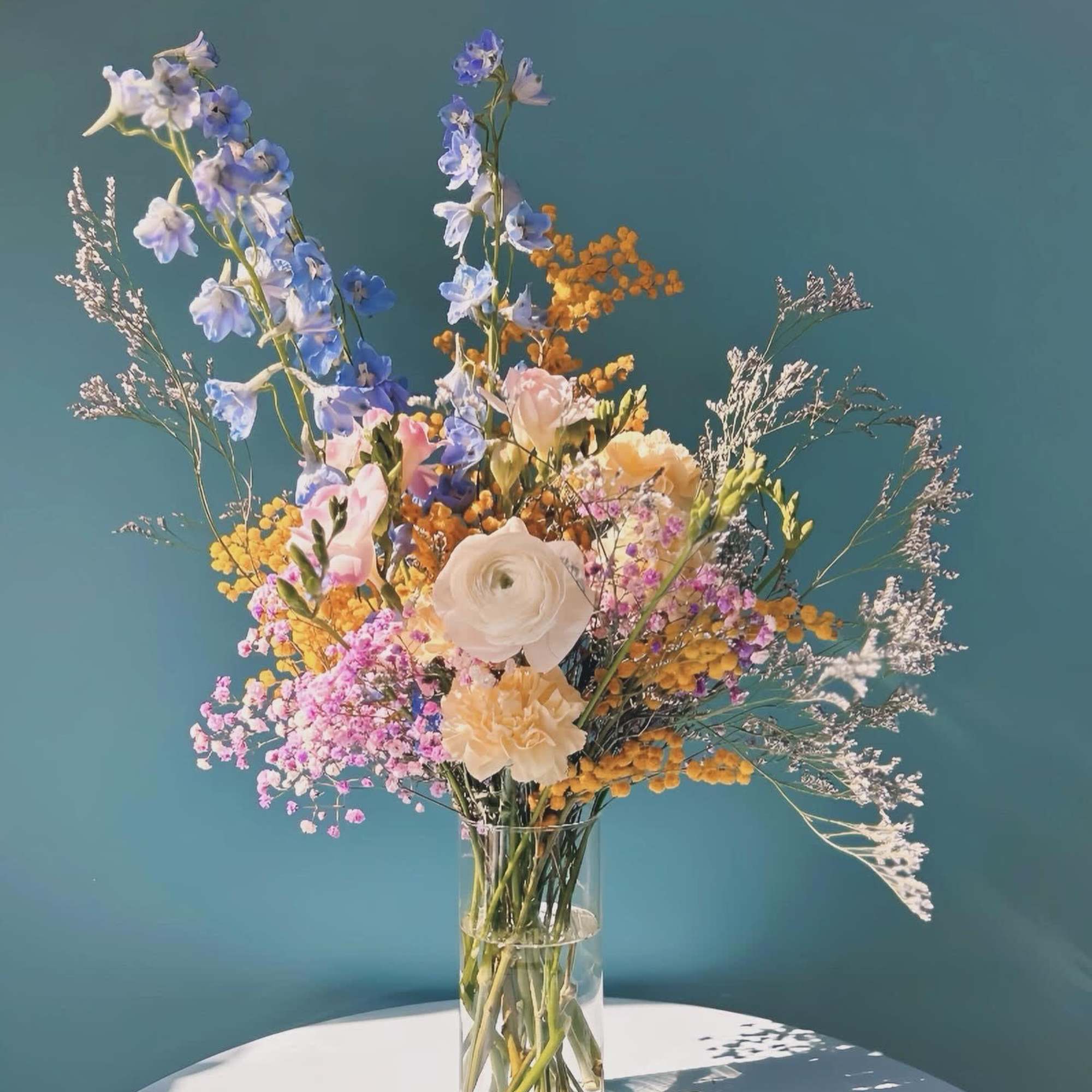 Tall mixed bouquet in a clear glass vase with blue, pink, and white flowers