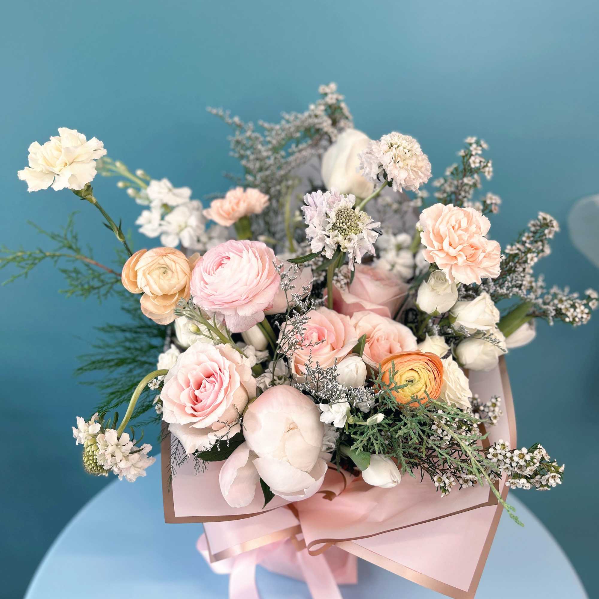 Pastel bouquet of pink, peach, and white flowers wrapped in pink paper