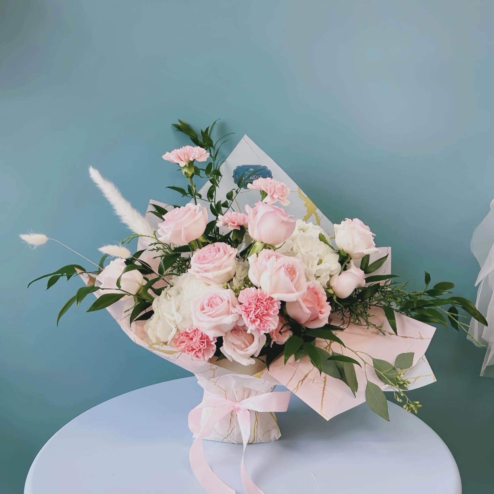 Pink roses and carnations arranged in pastel wrapping with a ribbon