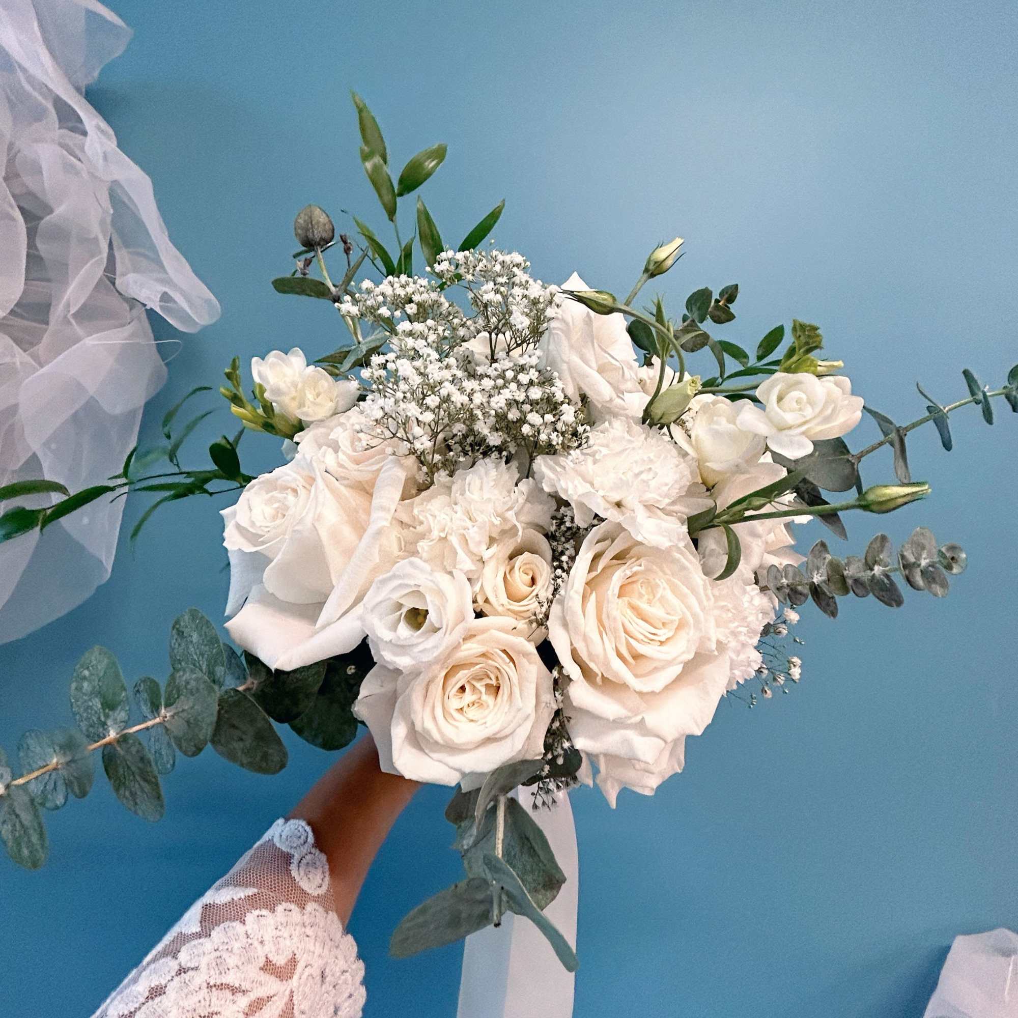 White bridal bouquet with roses and baby's breath, accented by eucalyptus