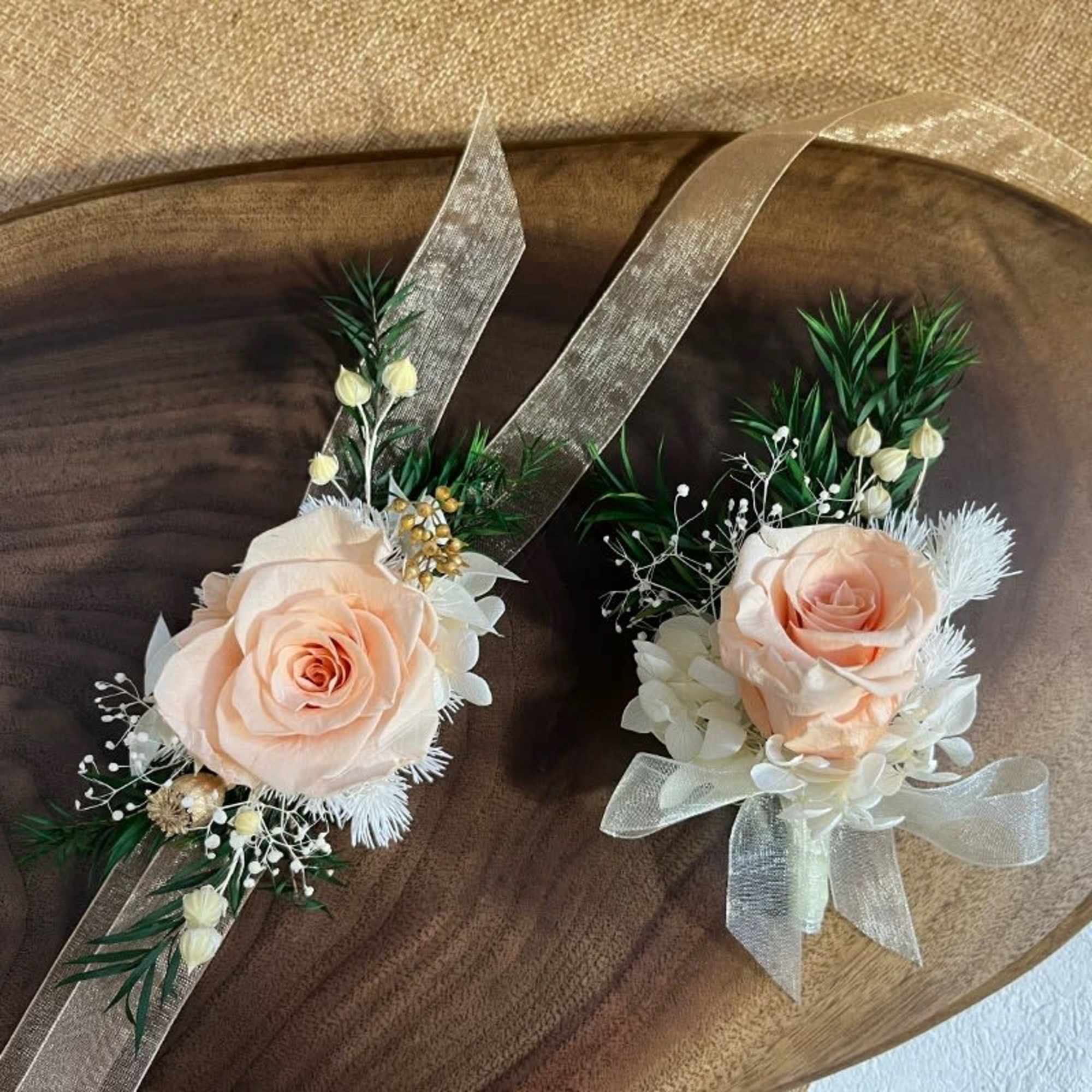 Two peach rose wrist corsages with ribbon and greenery