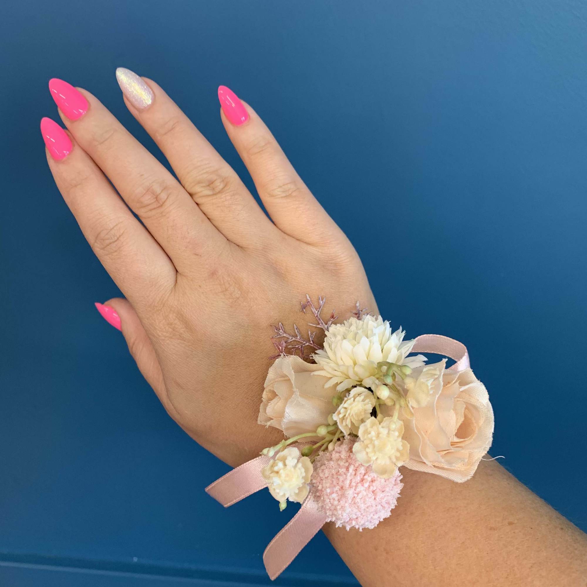 Floral wrist corsage with pale peach and pink flowers on a hand