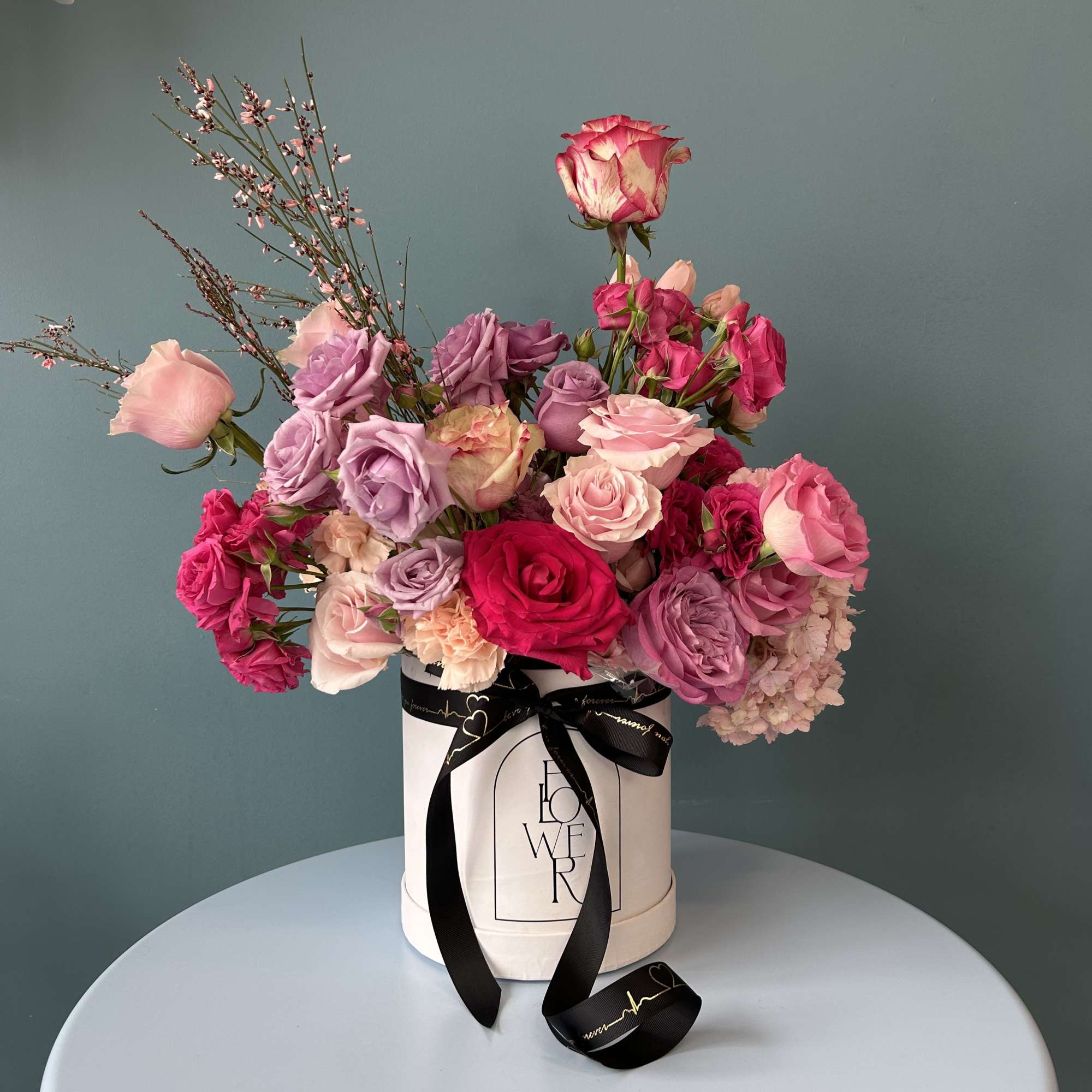Pink and lavender roses arranged in a white hat box with a black ribbon
