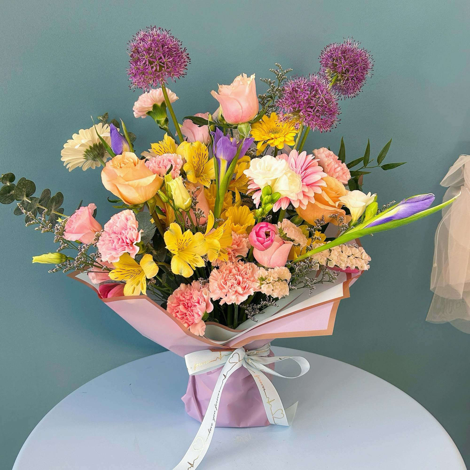 Mixed bouquet of pink, yellow, purple, and white flowers wrapped in pastel paper