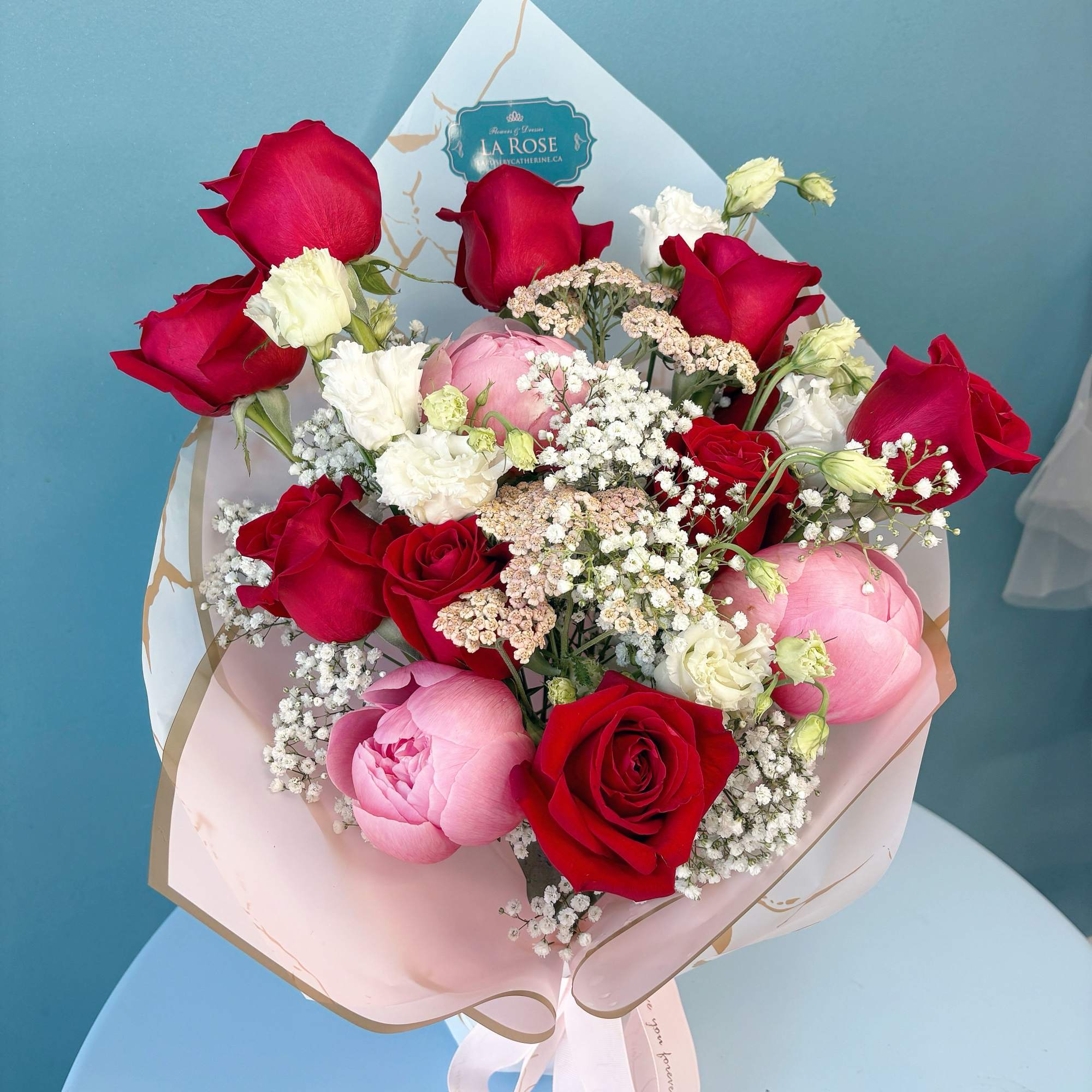 Bouquet of red roses, pink peonies, and white filler flowers in pastel wrapping