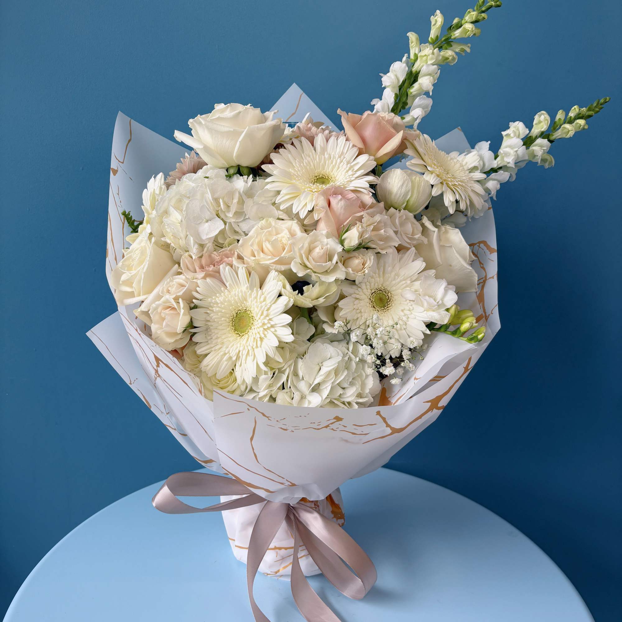 Bouquet of white and blush flowers wrapped in white paper with a ribbon