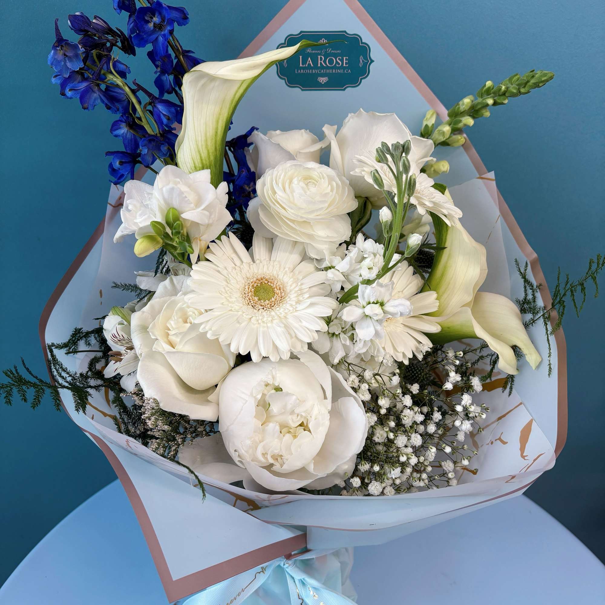 White bouquet with blue flowers and calla lilies wrapped in pale paper