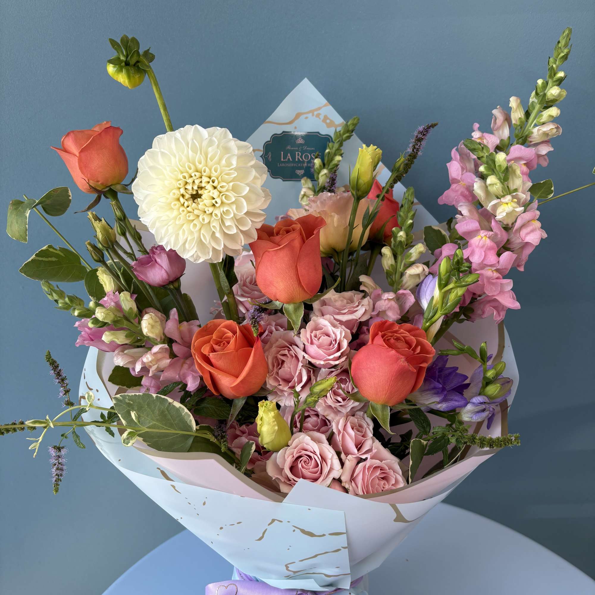 Mixed bouquet of coral and pink roses with a white dahlia in pastel wrap