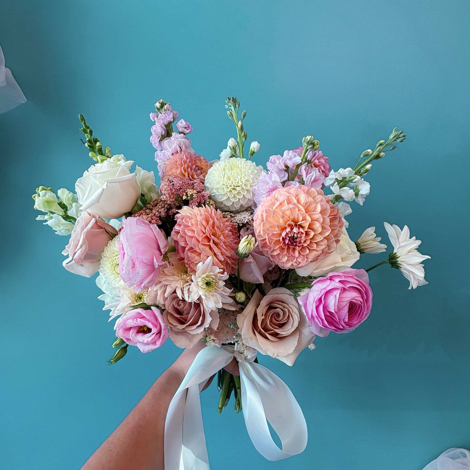 Hand-tied bouquet of pink, peach, and white flowers with a white ribbon
