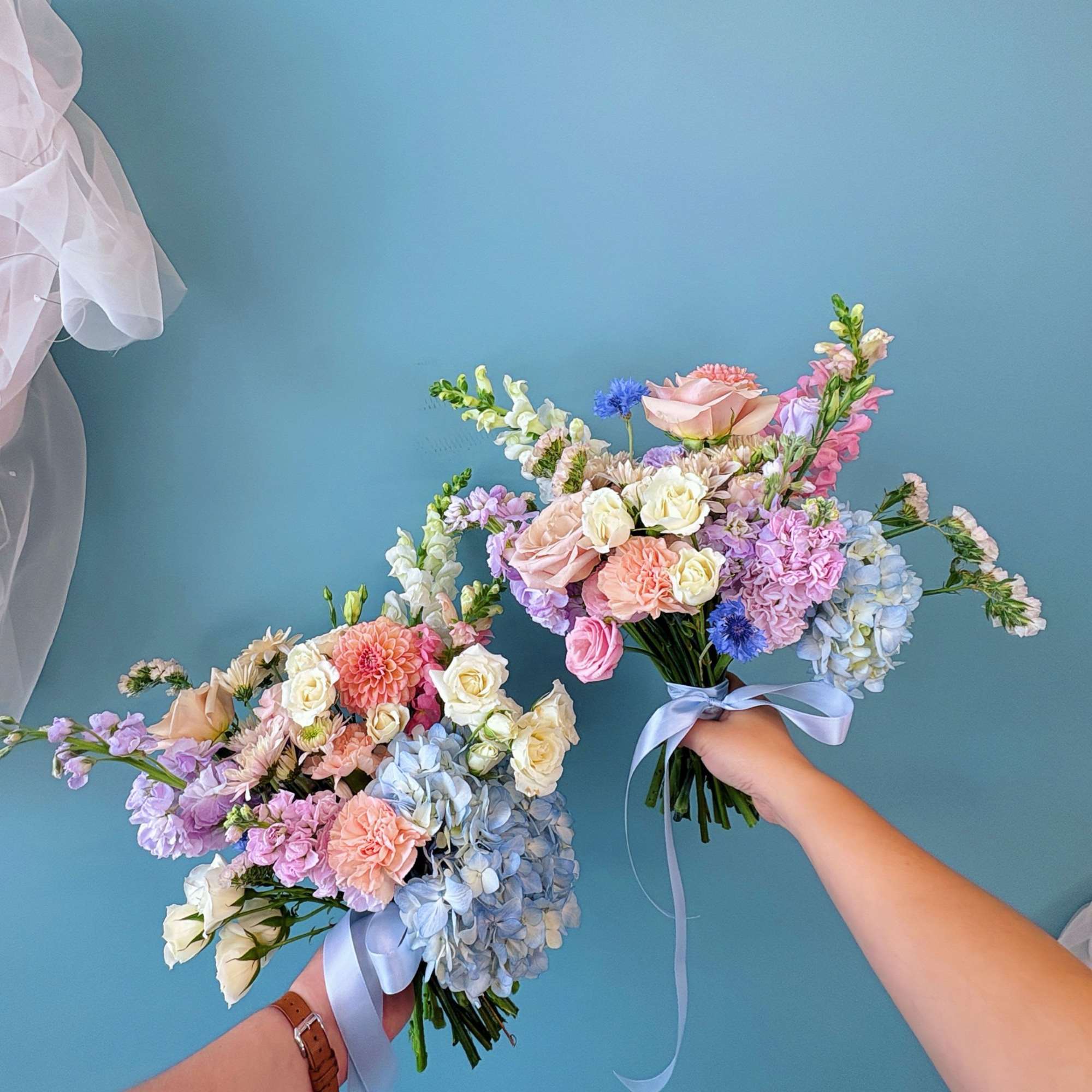 Two pastel wedding bouquets with roses, hydrangeas, and ribbon ties